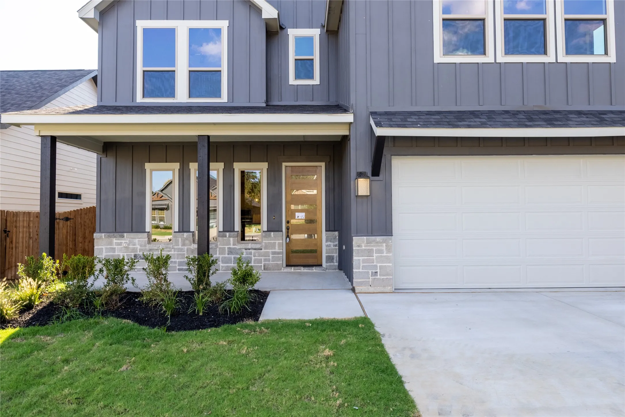 Modern exterior featuring vertical siding, stone accents, a covered entry, and an integrated garage