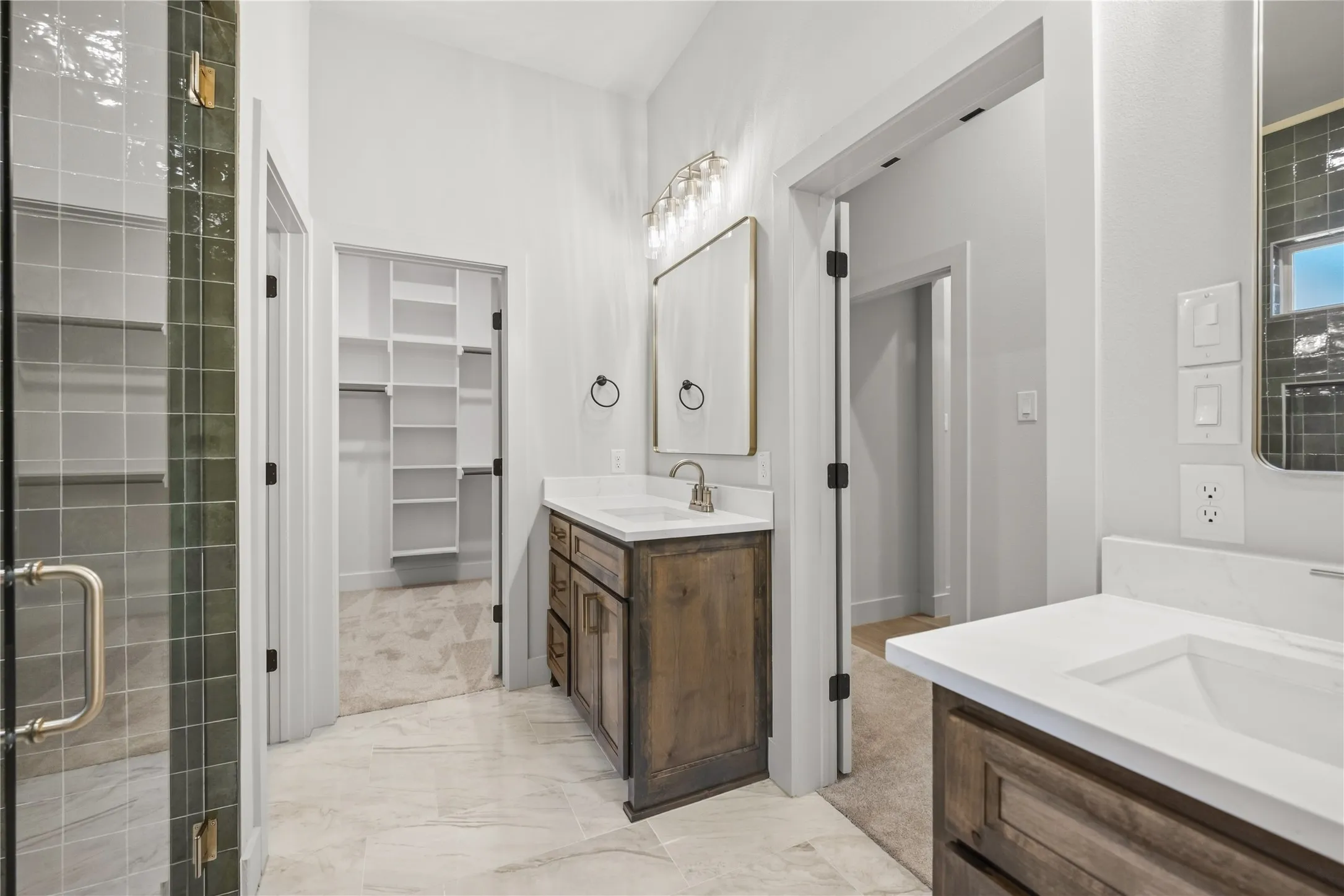 Dual vanity sinks with white countertops, wood-finish cabinetry, a walk-in shower with tiled walls and a glass enclosure, and a walk-in closet with built-in shelving