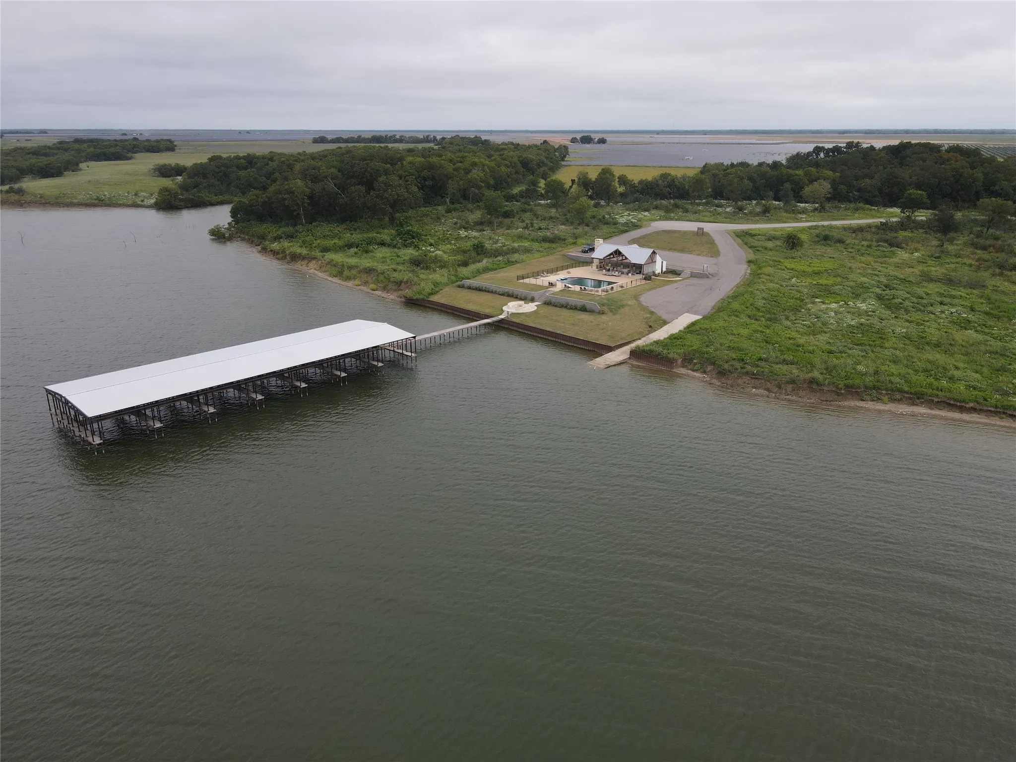 Waterfront property featuring a private boat dock with multiple slips, a dedicated boat ramp, a residence with an outdoor pool, and extensive natural landscaping