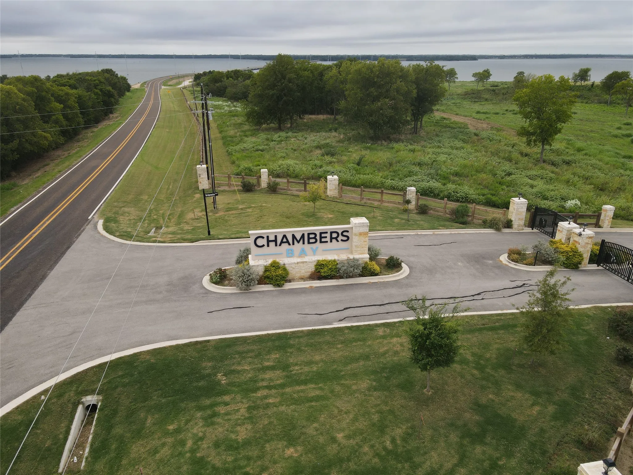 Gated community entrance featuring a stone sign, paved roadways, and landscaped grounds