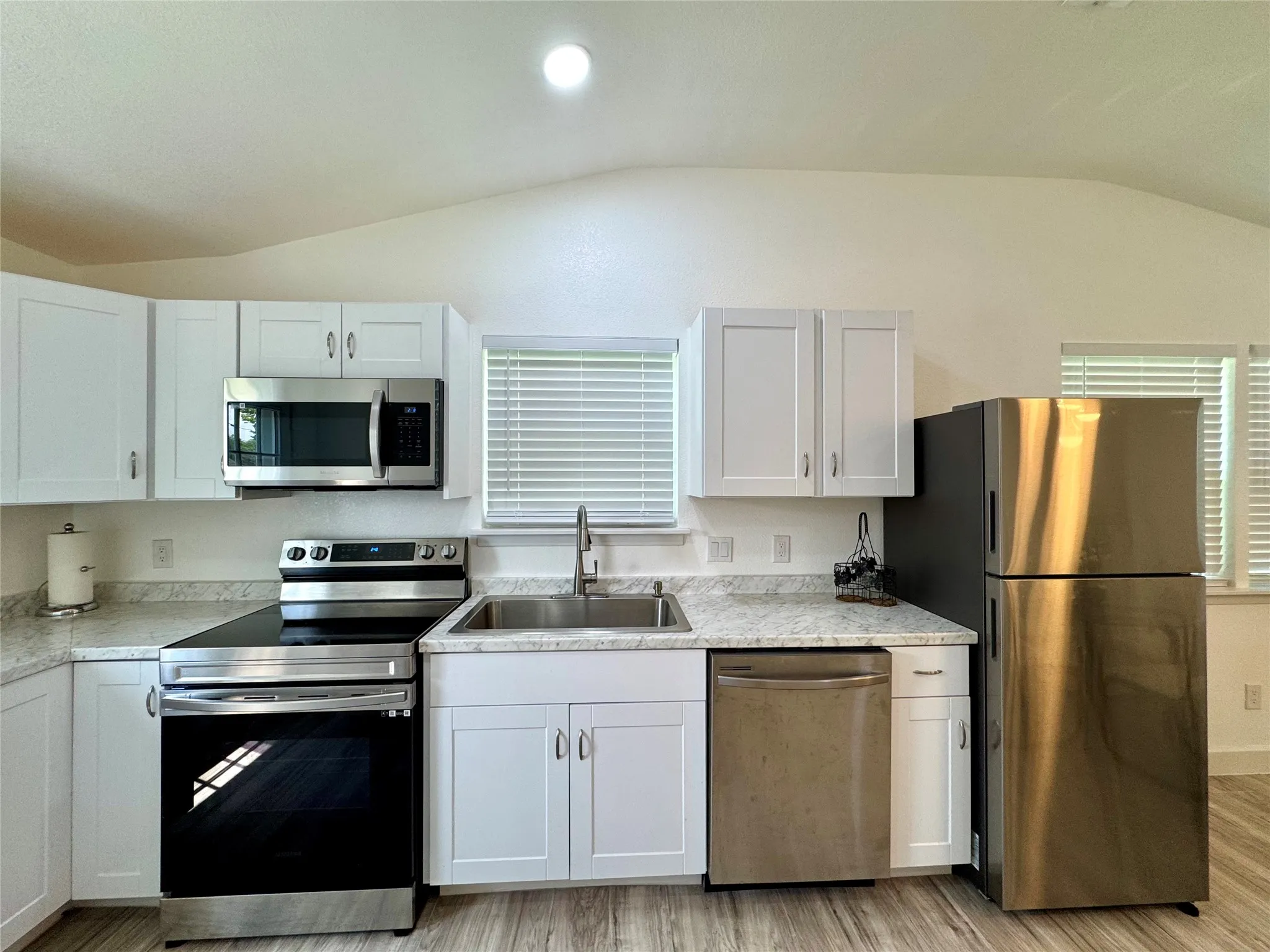 Kitchen with appliances with stainless steel finishes, lofted ceiling, light wood-style flooring, light countertops, and white cabinets