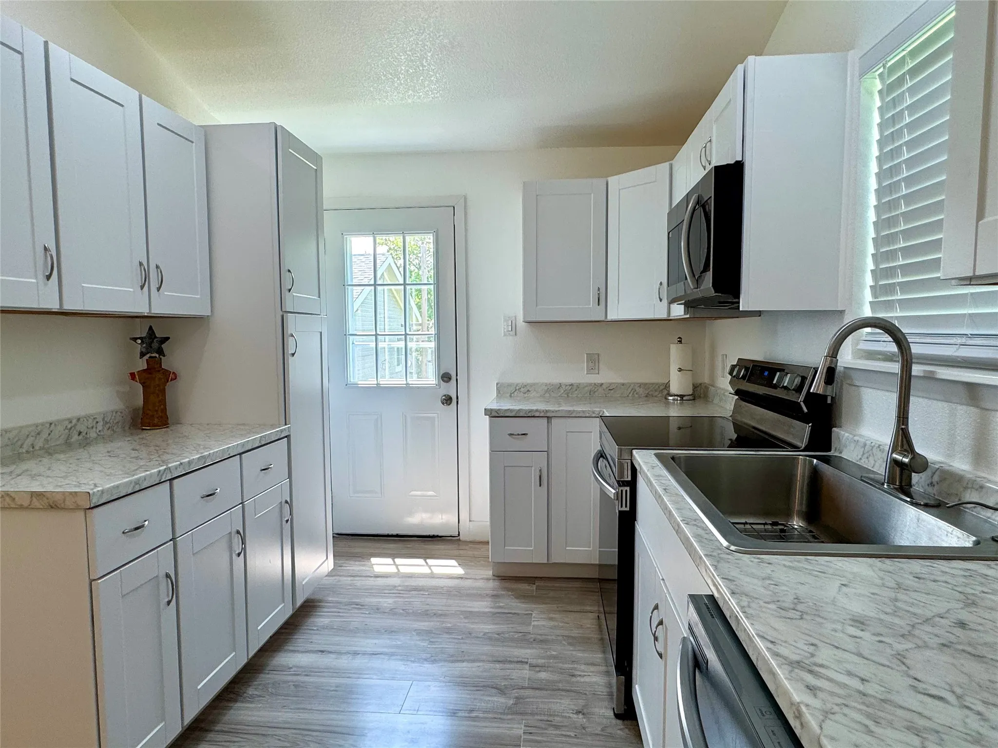 Kitchen with stainless steel appliances, light countertops, light wood finished floors, and white cabinetry