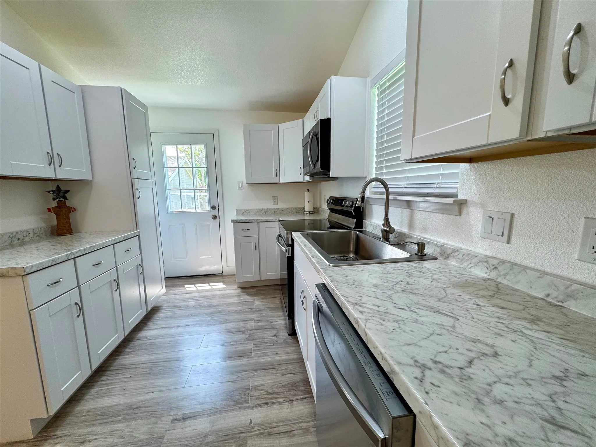 Kitchen with stainless steel appliances, light countertops, light wood finished floors, and a textured ceiling