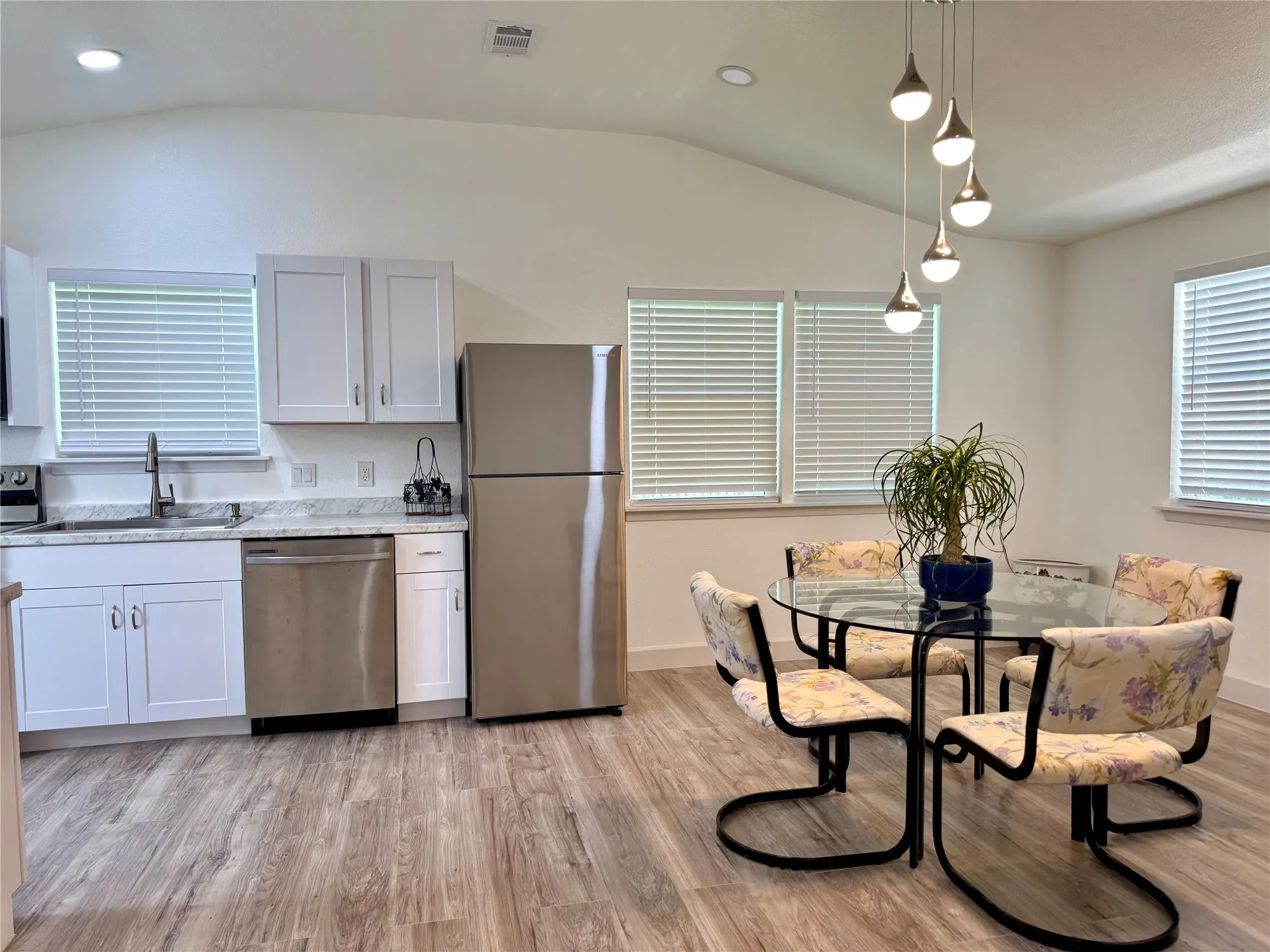 Kitchen with appliances with stainless steel finishes, vaulted ceiling, light wood-style flooring, light stone counters, and decorative light fixtures