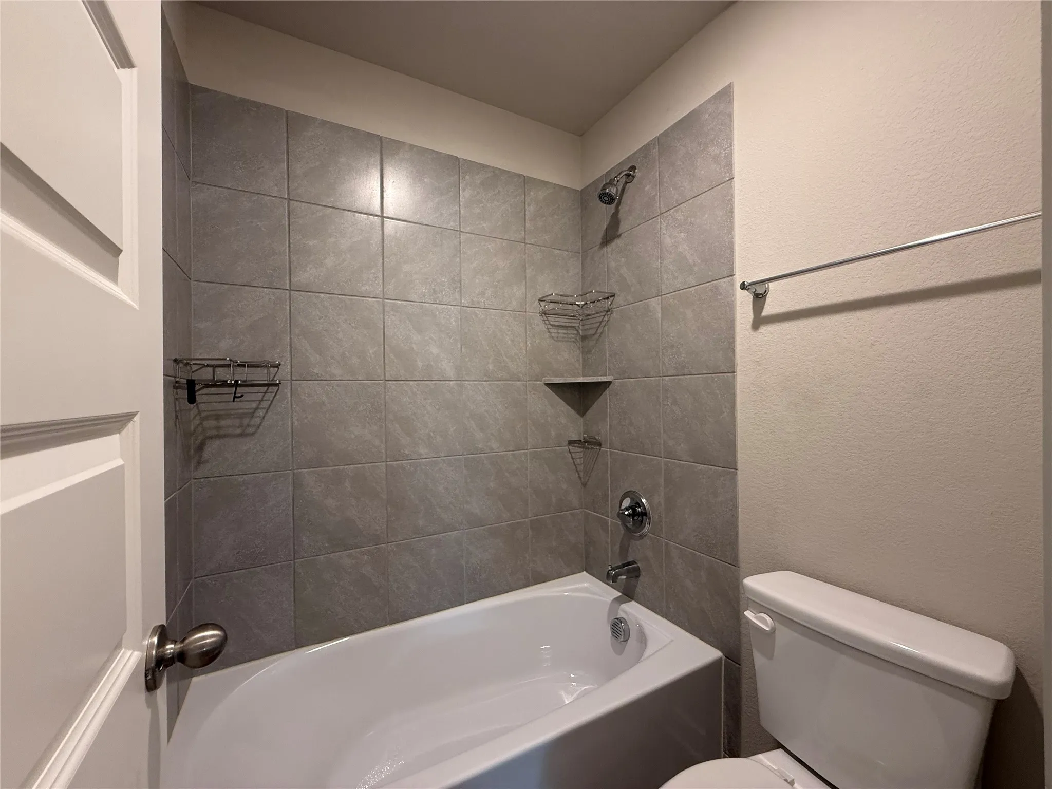 Bathtub with gray subway tile surround, chrome fixtures, and built-in shelving