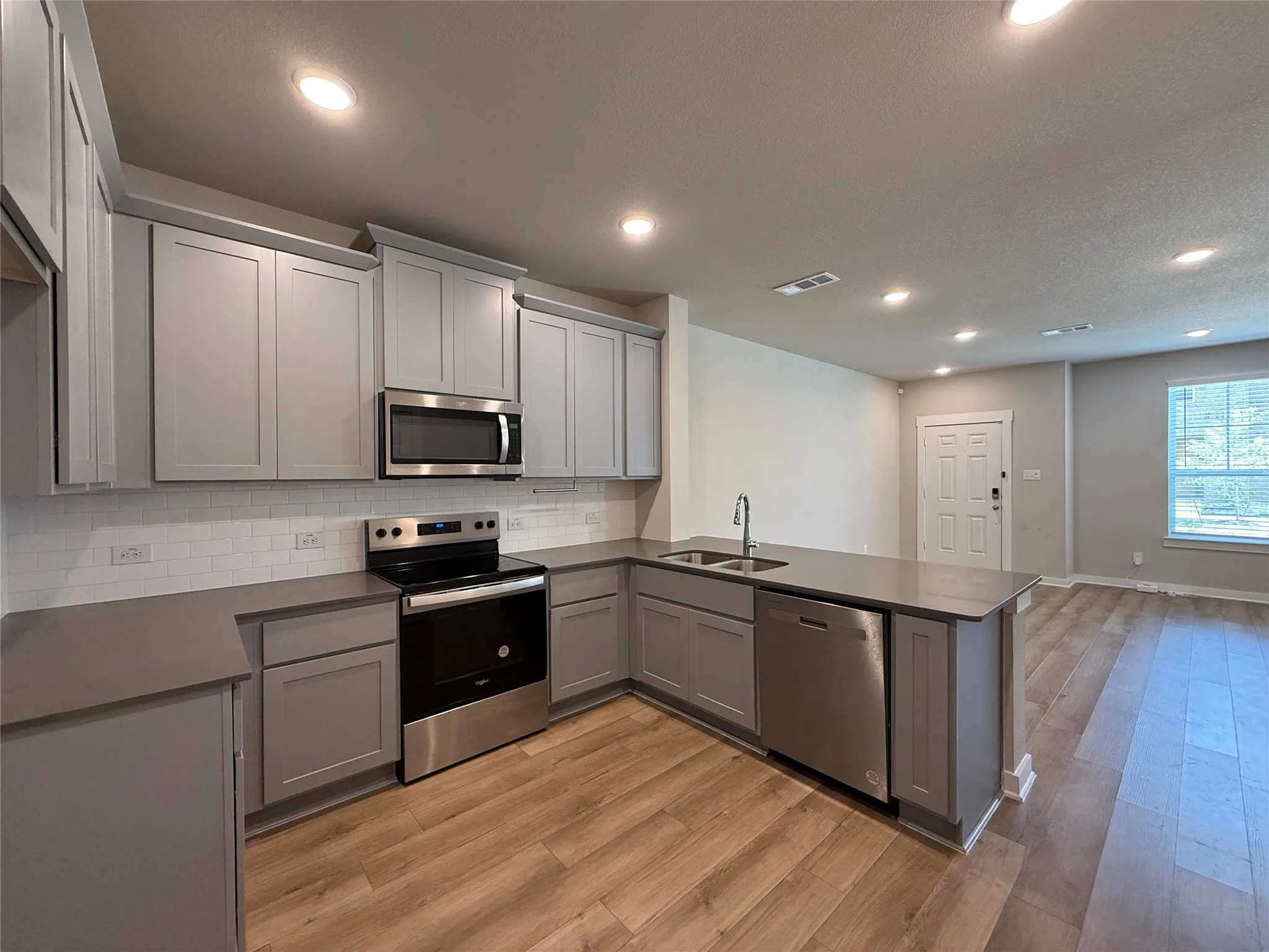 Modern kitchen featuring light gray cabinetry, stainless steel appliances, a white subway tile backsplash, and wood-finish flooring