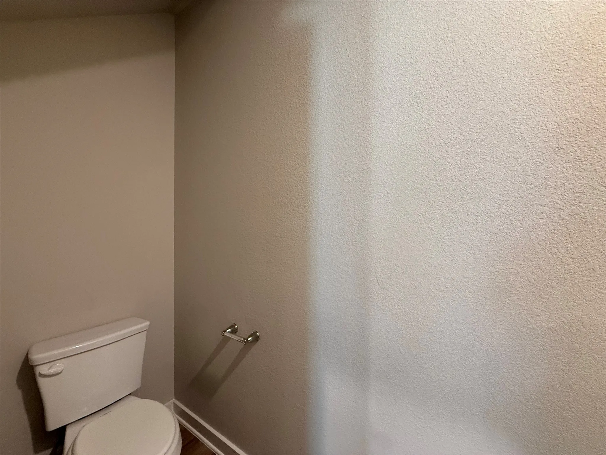 White ceramic toilet with a dual-flush mechanism, chrome towel bar, and wood-finish flooring