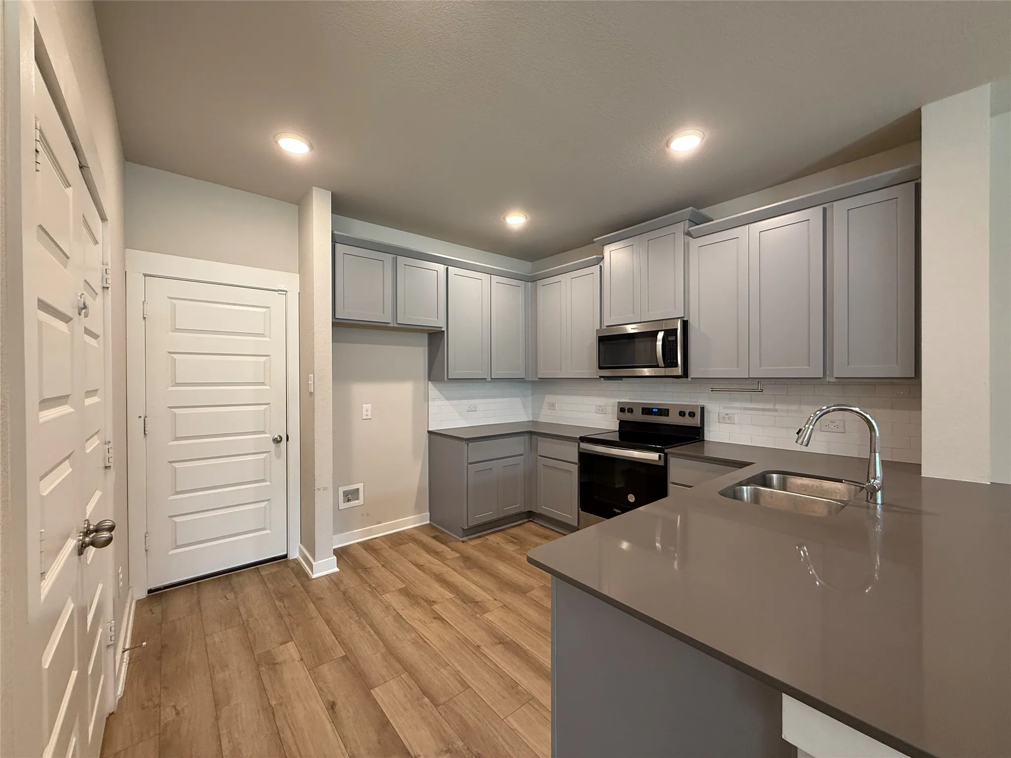 Kitchen with wood-finish flooring, recessed lighting, gray cabinetry, stainless steel appliances, and a double basin sink