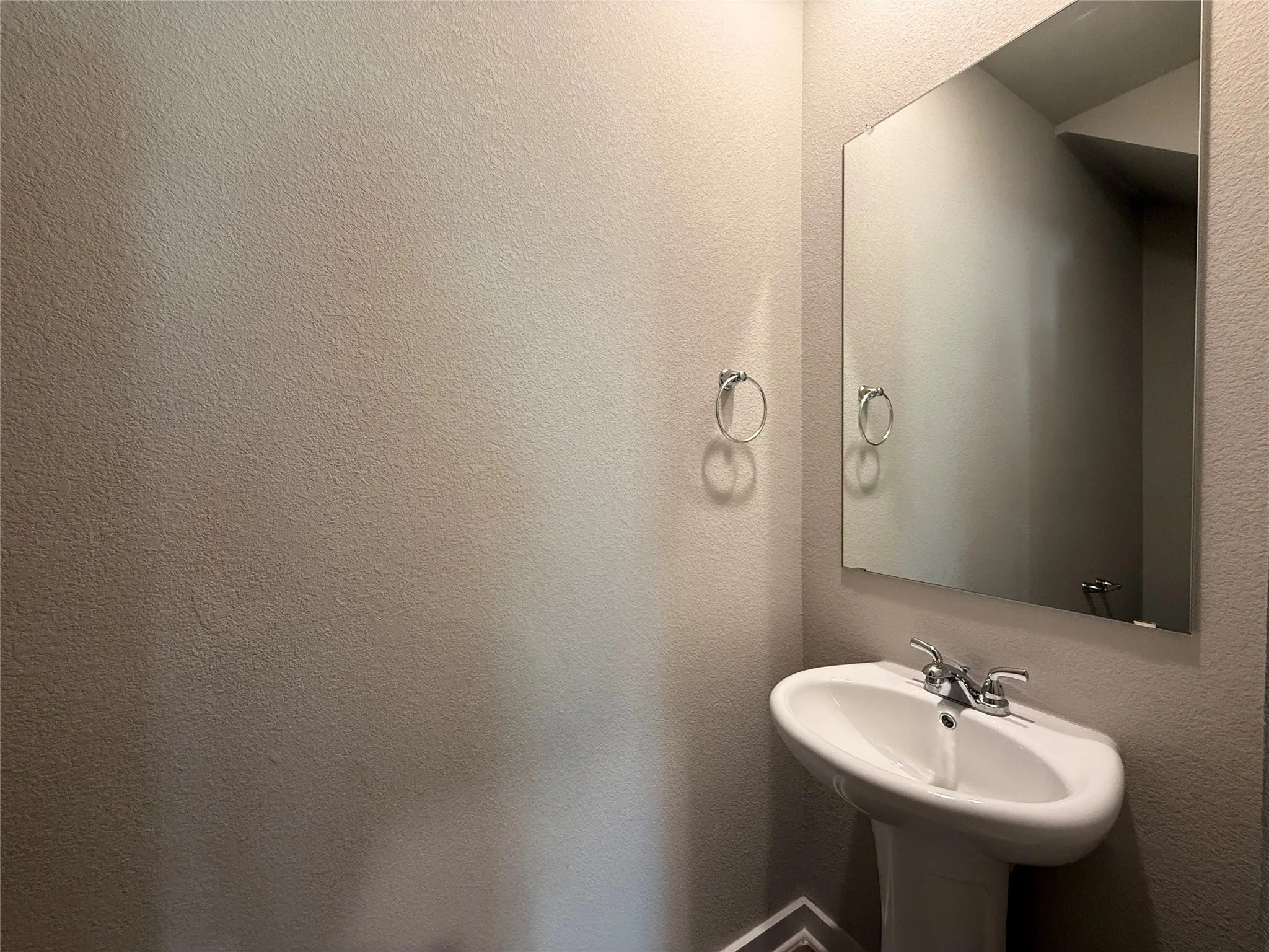 Pedestal sink with a two-handle chrome faucet, rectangular mirror, and light-toned walls