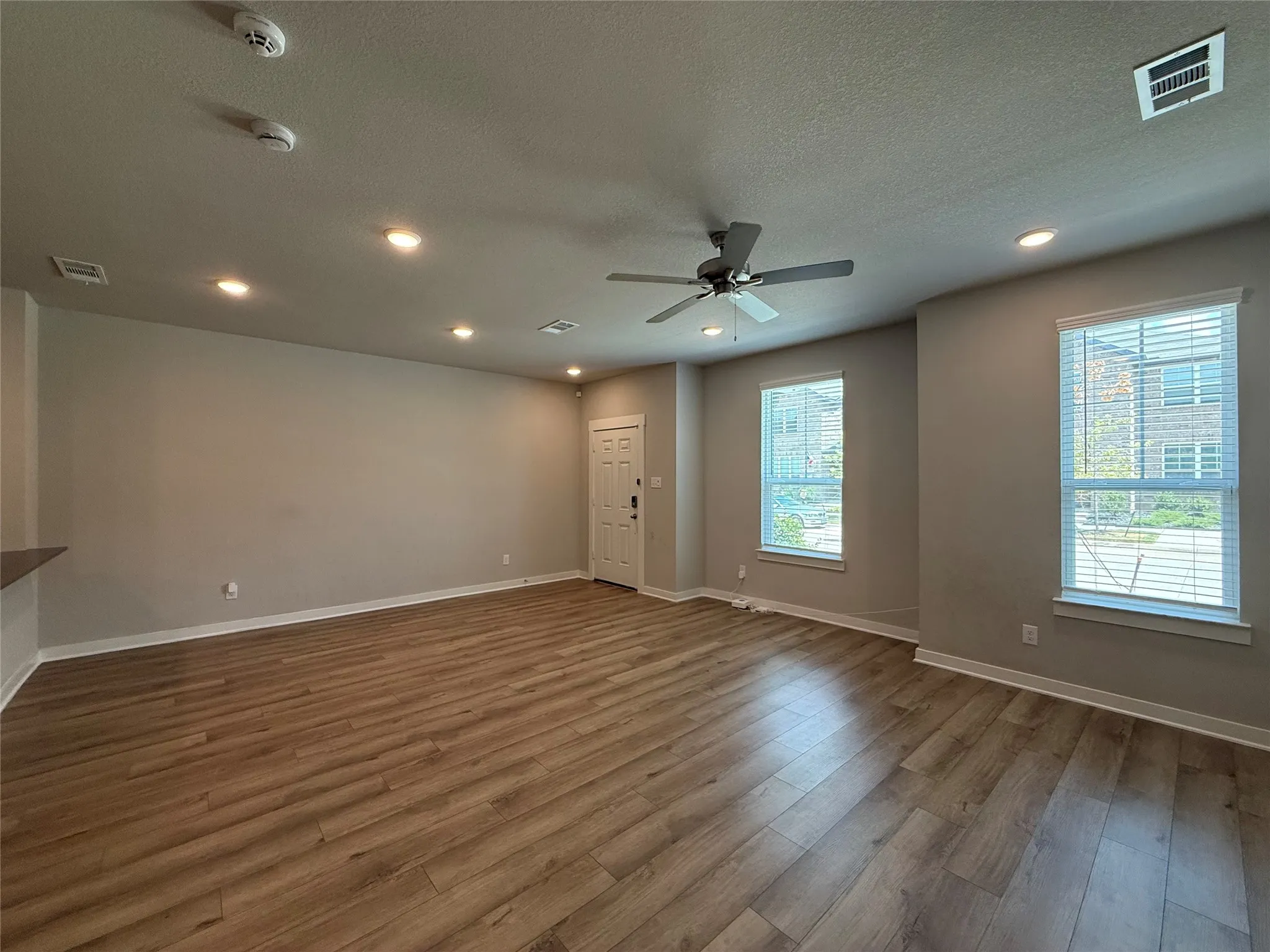 Wood-finish flooring, recessed lighting, ceiling fan, and multiple windows with blinds