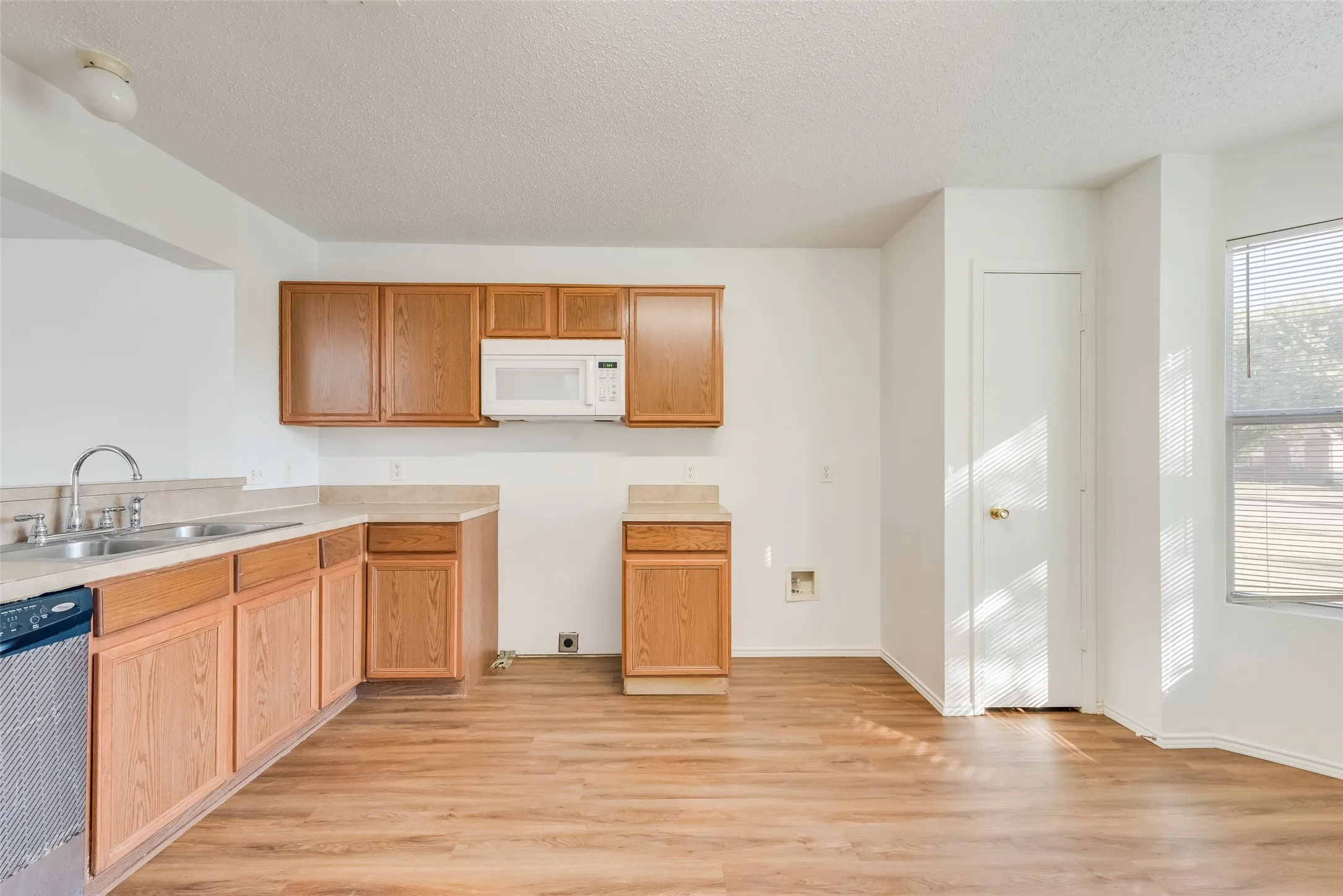 Kitchen featuring wood-finish cabinetry, a double basin sink with a gooseneck faucet, light-toned countertops, and wood-finish flooring
