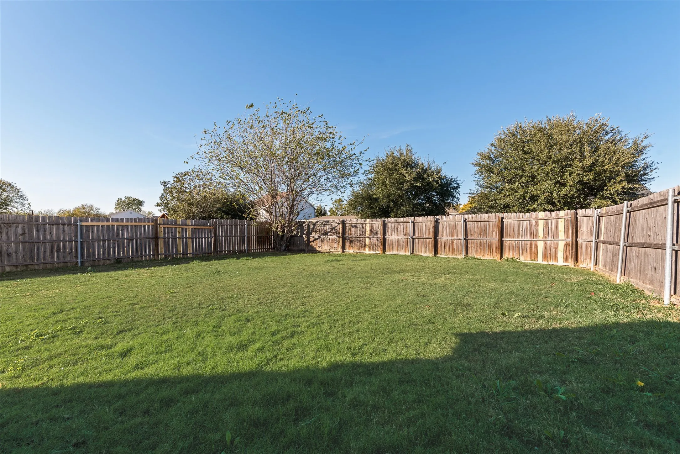 Expansive grassy area featuring a perimeter wood fence and mature trees