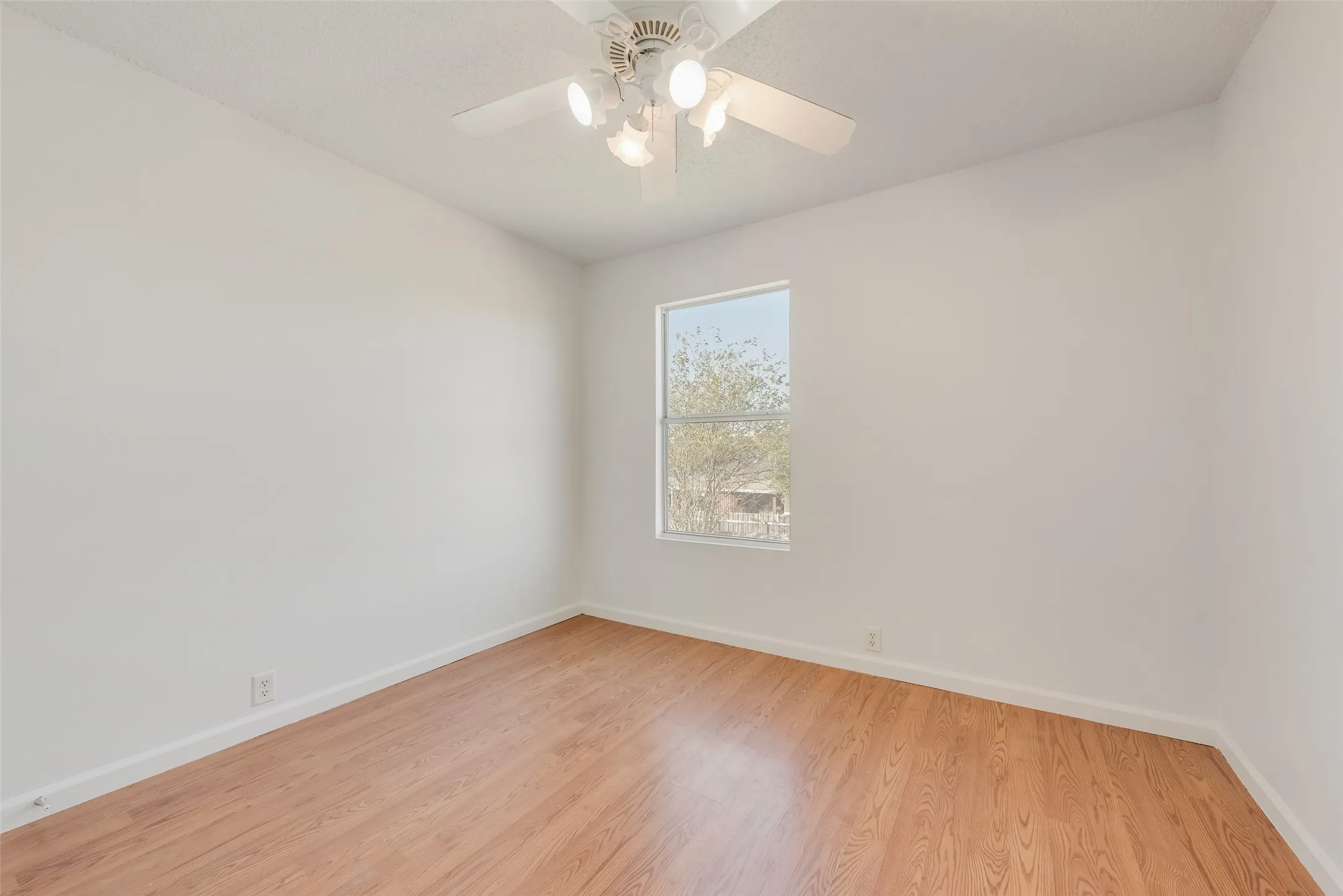 Light-filled room featuring wood-finish flooring, white walls, a window, and a ceiling fan with integrated lighting
