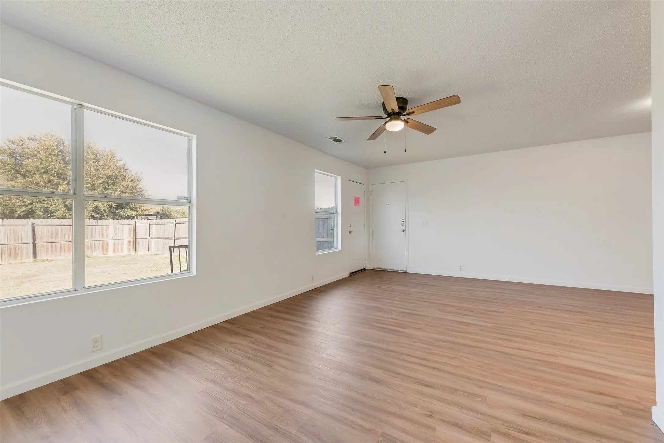 Expansive interior space featuring wood-finish flooring, a ceiling fan with light fixture, white walls, and multiple windows