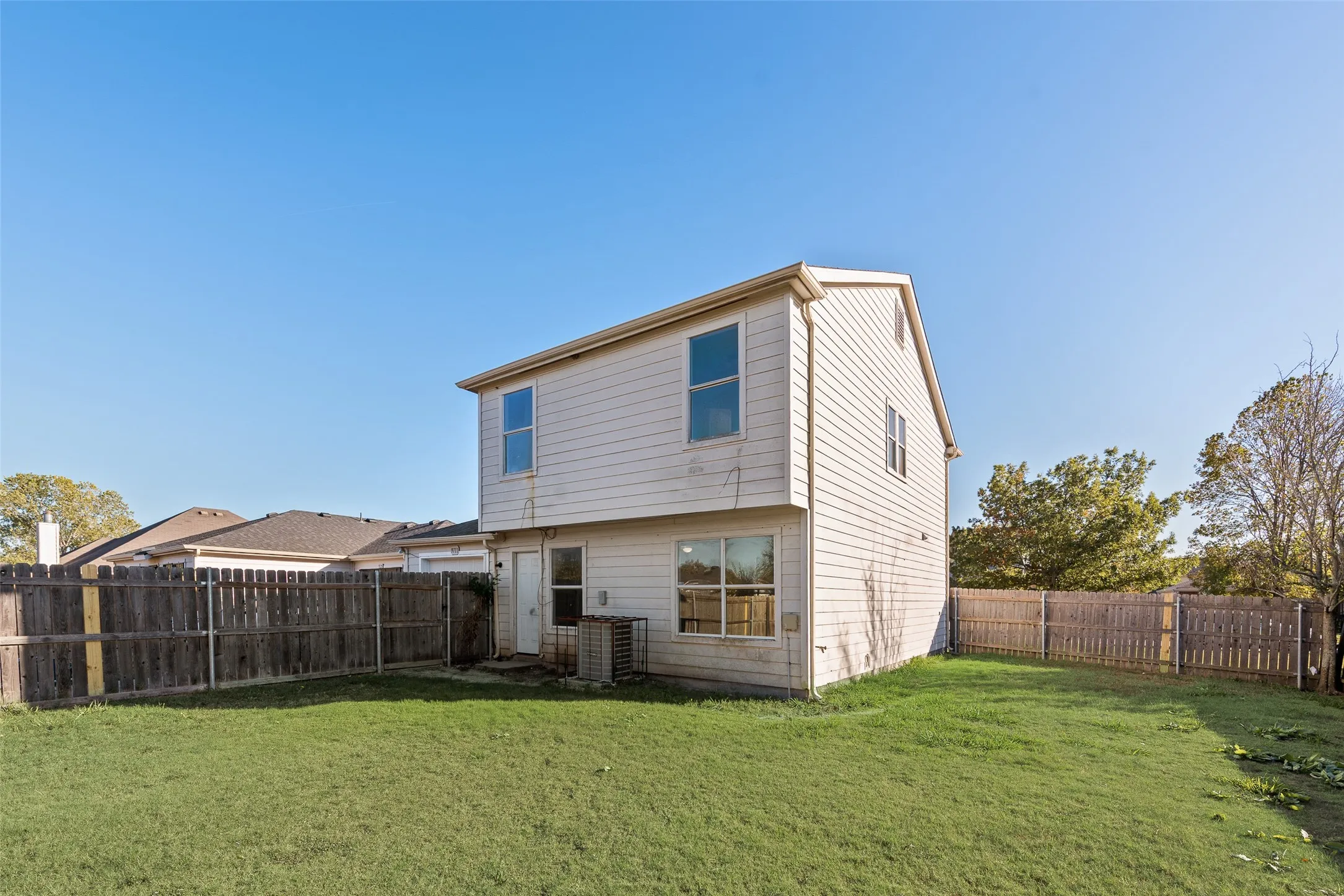 Expansive backyard featuring a manicured lawn, full privacy fencing, and a two-story home exterior with multiple windows