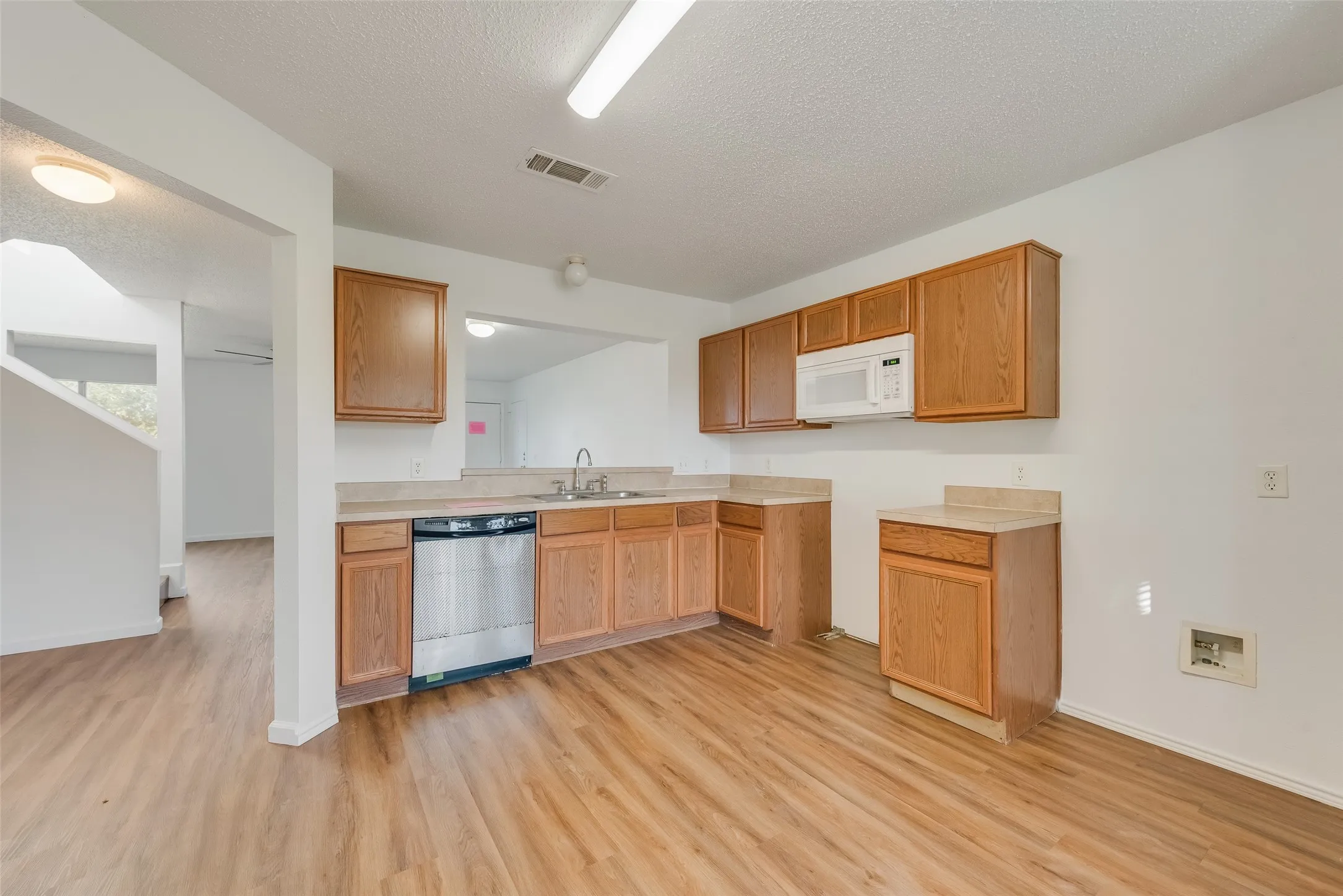 Kitchen featuring wood-finish flooring, wood cabinetry, a stainless steel dishwasher, a built-in microwave, and laminate countertops