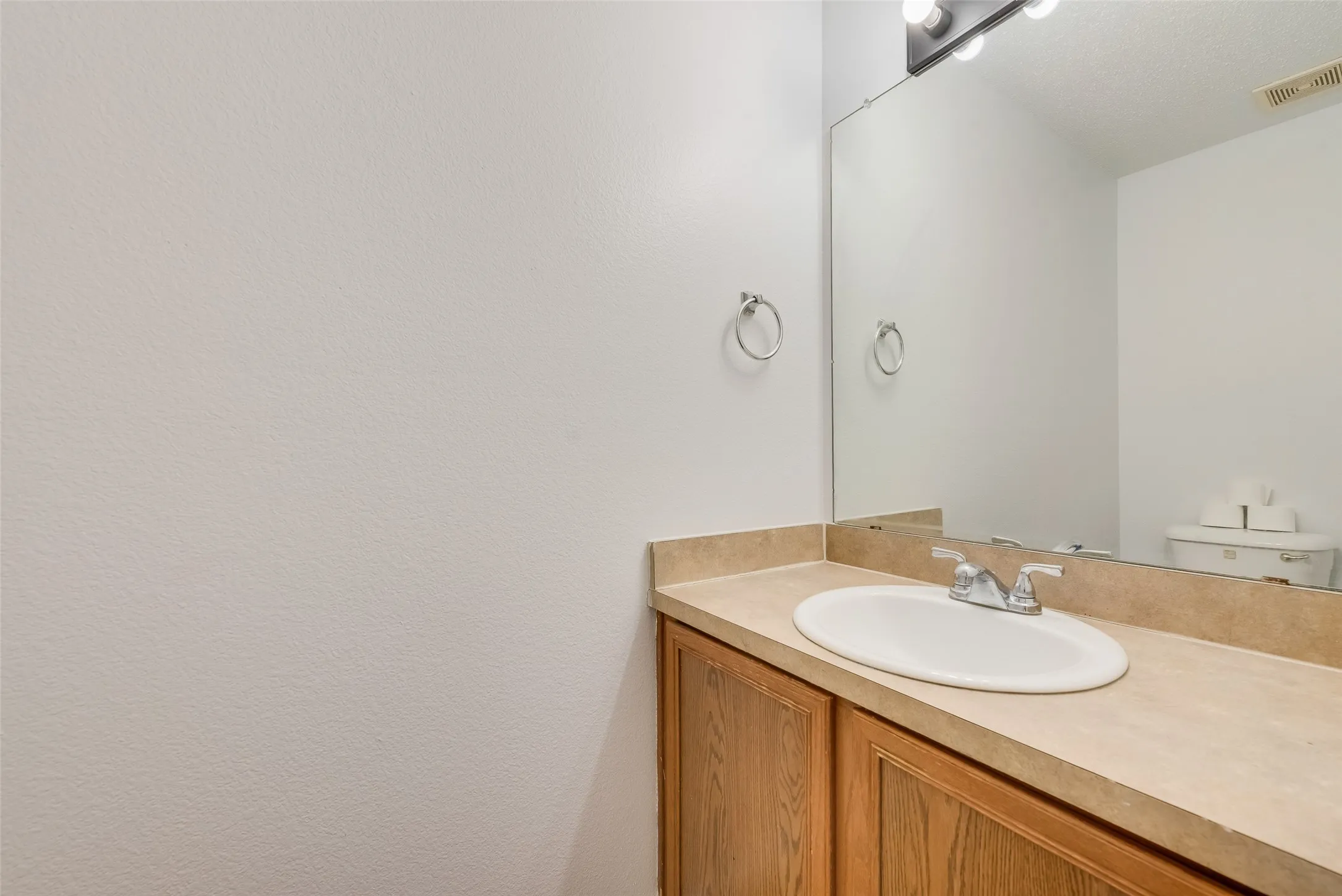 Vanity with wood-finish cabinetry, integrated sink, and a mounted mirror