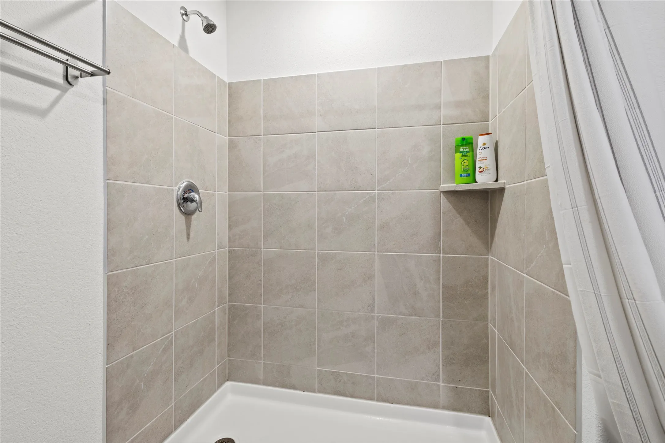 Tiled shower enclosure featuring a built-in shelf, showerhead, and chrome fixture