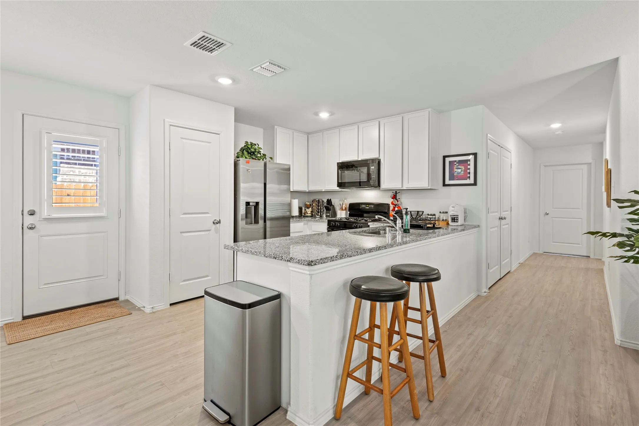 Kitchen featuring light-tone wood-finish flooring, white cabinetry, granite countertops, and recessed lighting