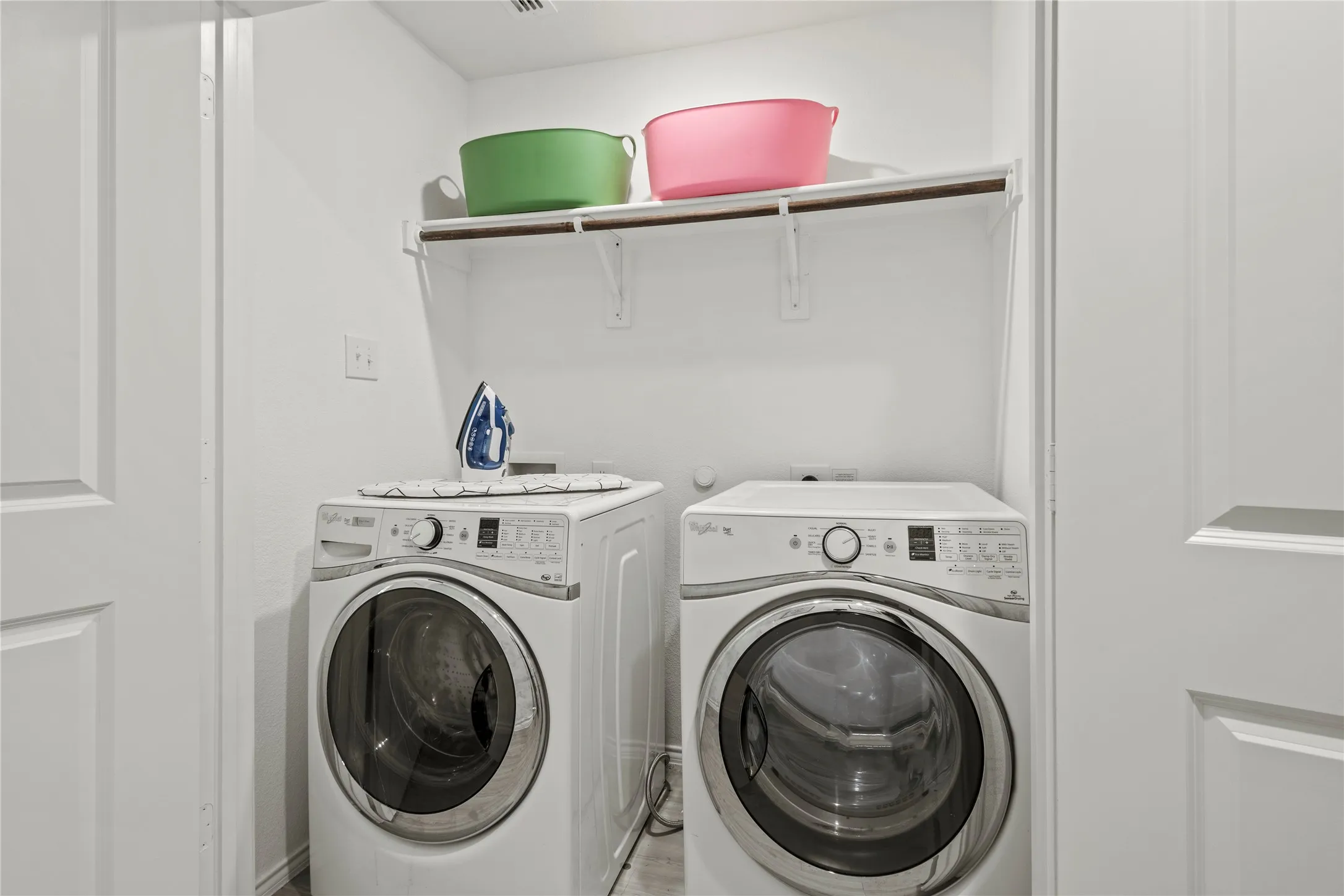 Dedicated laundry space with built-in shelving, white paneled doors, and a wood-finish flooring