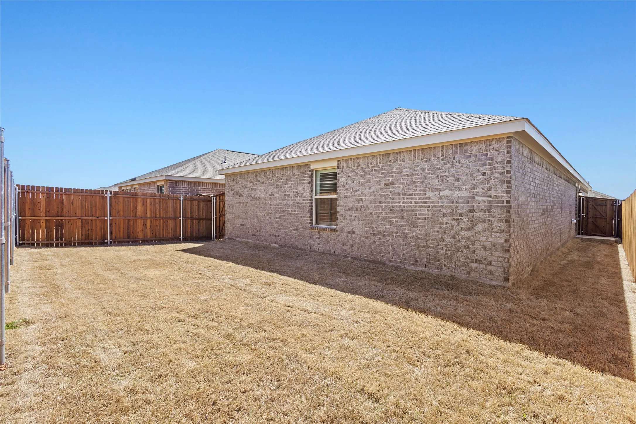 Brick exterior with a shingle roof and a secured wood fence