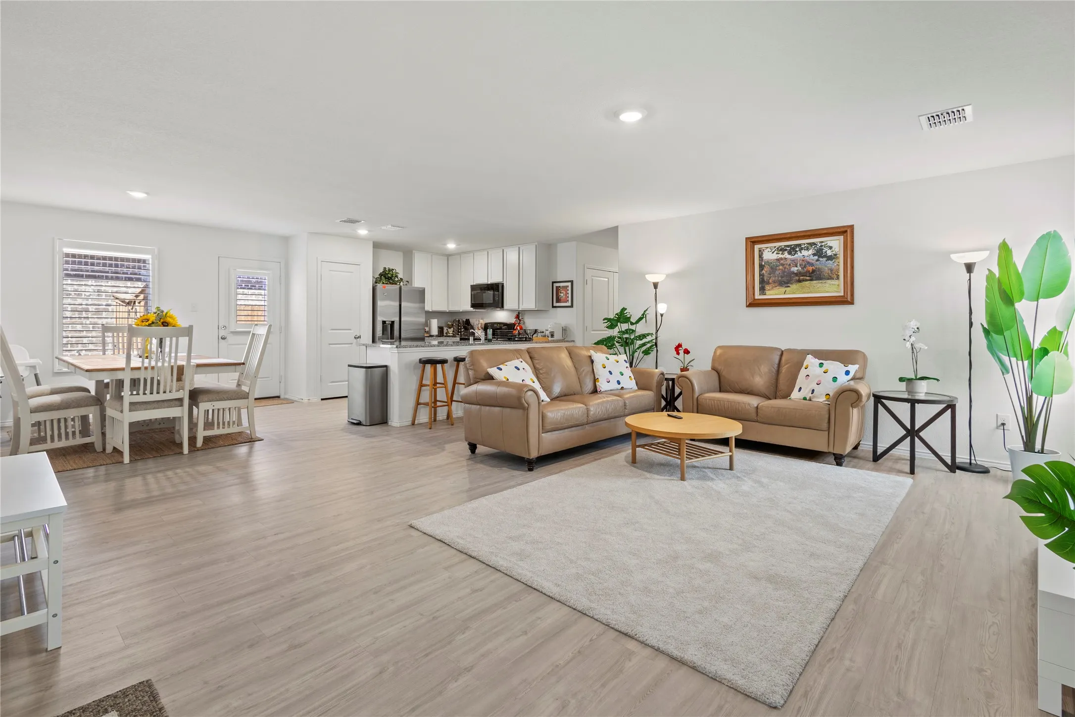 Open-concept living area featuring wood-finish flooring, recessed lighting, and a kitchen with white cabinetry and stainless steel appliances