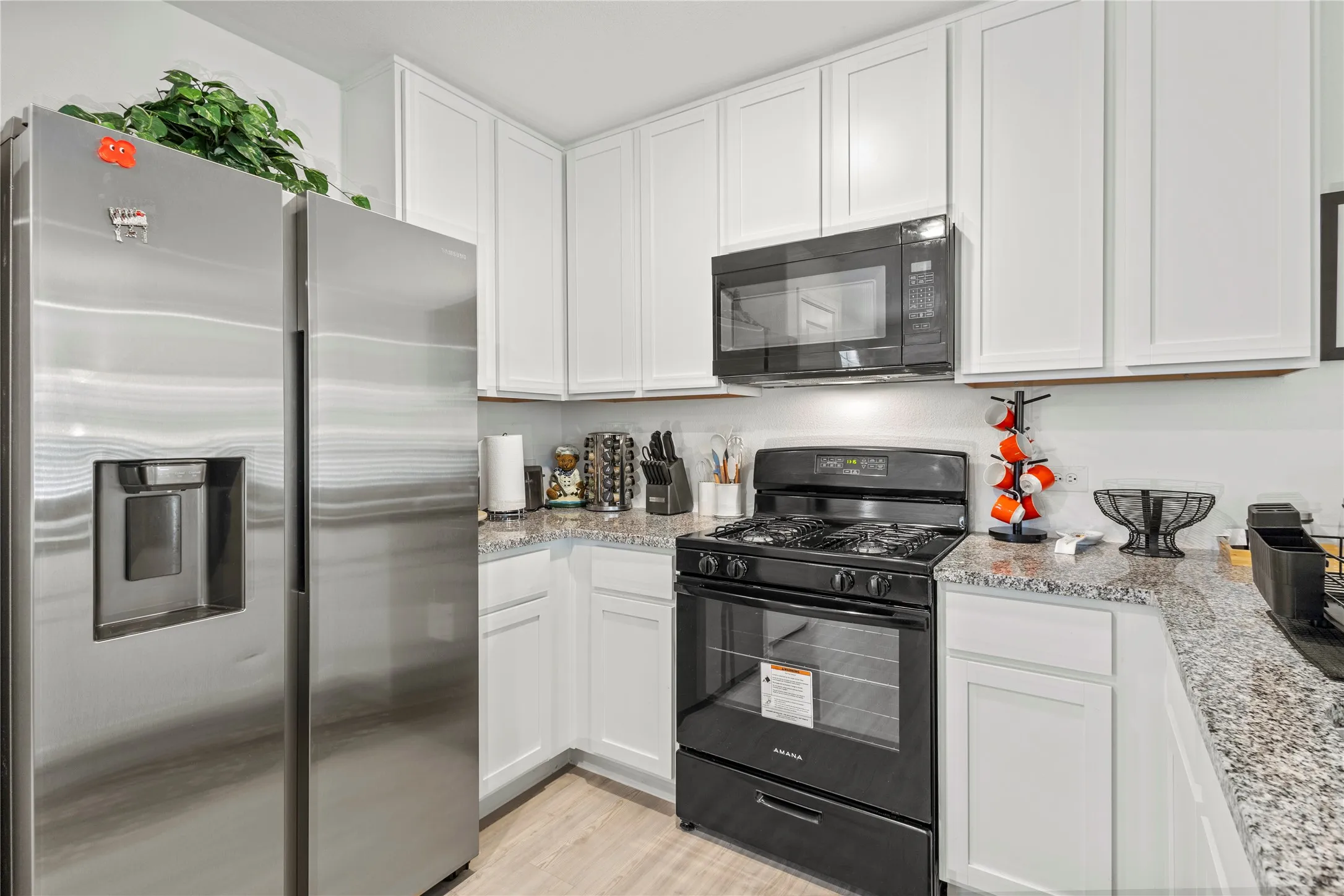White cabinetry, stainless steel side-by-side refrigerator, black range, black microwave, and wood-finish flooring