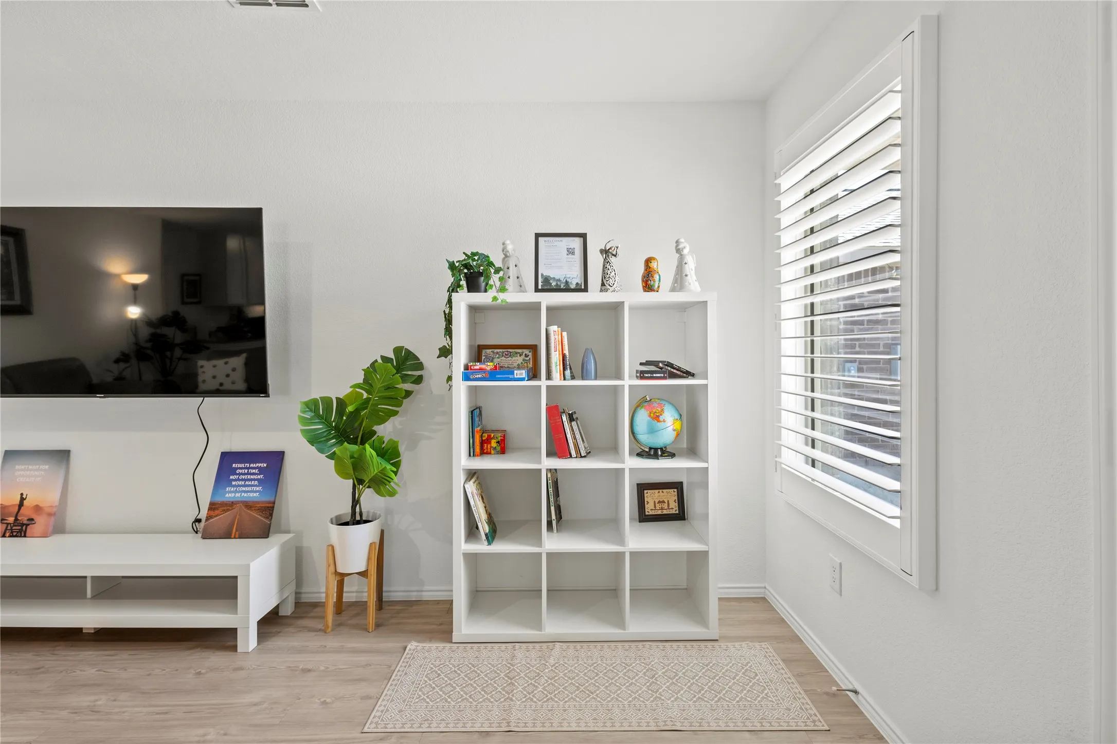 Wood-finish flooring, white walls, and a window with plantation shutters
