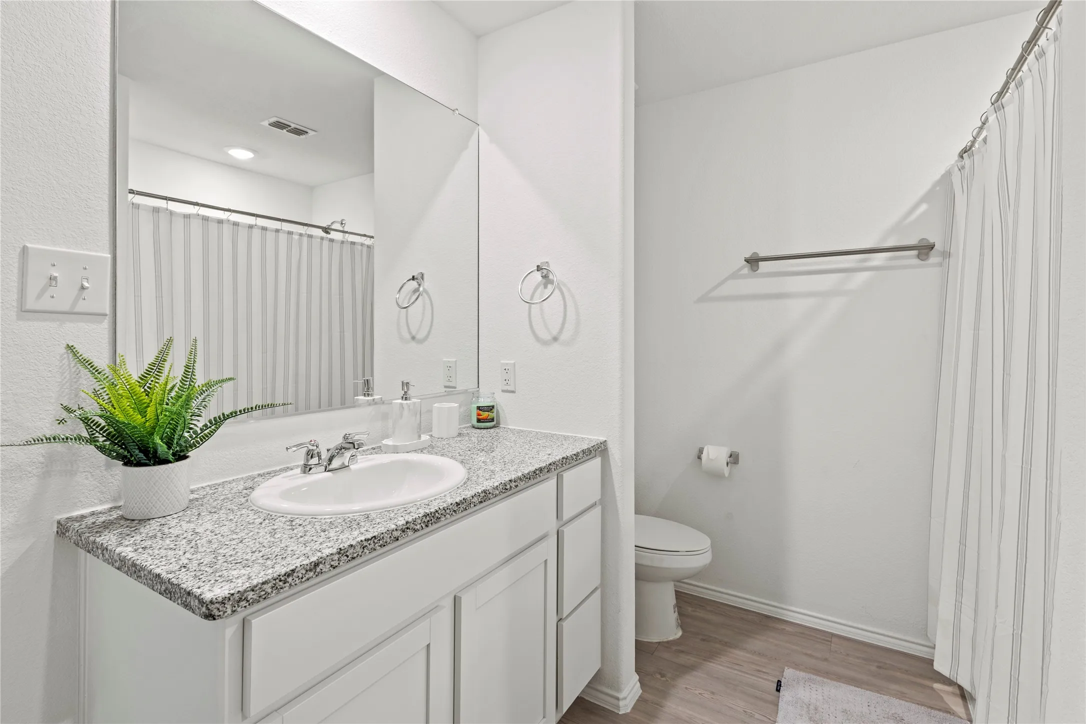 White wood-finish vanity with a drop-in sink, speckled countertop, and wall-mounted mirror