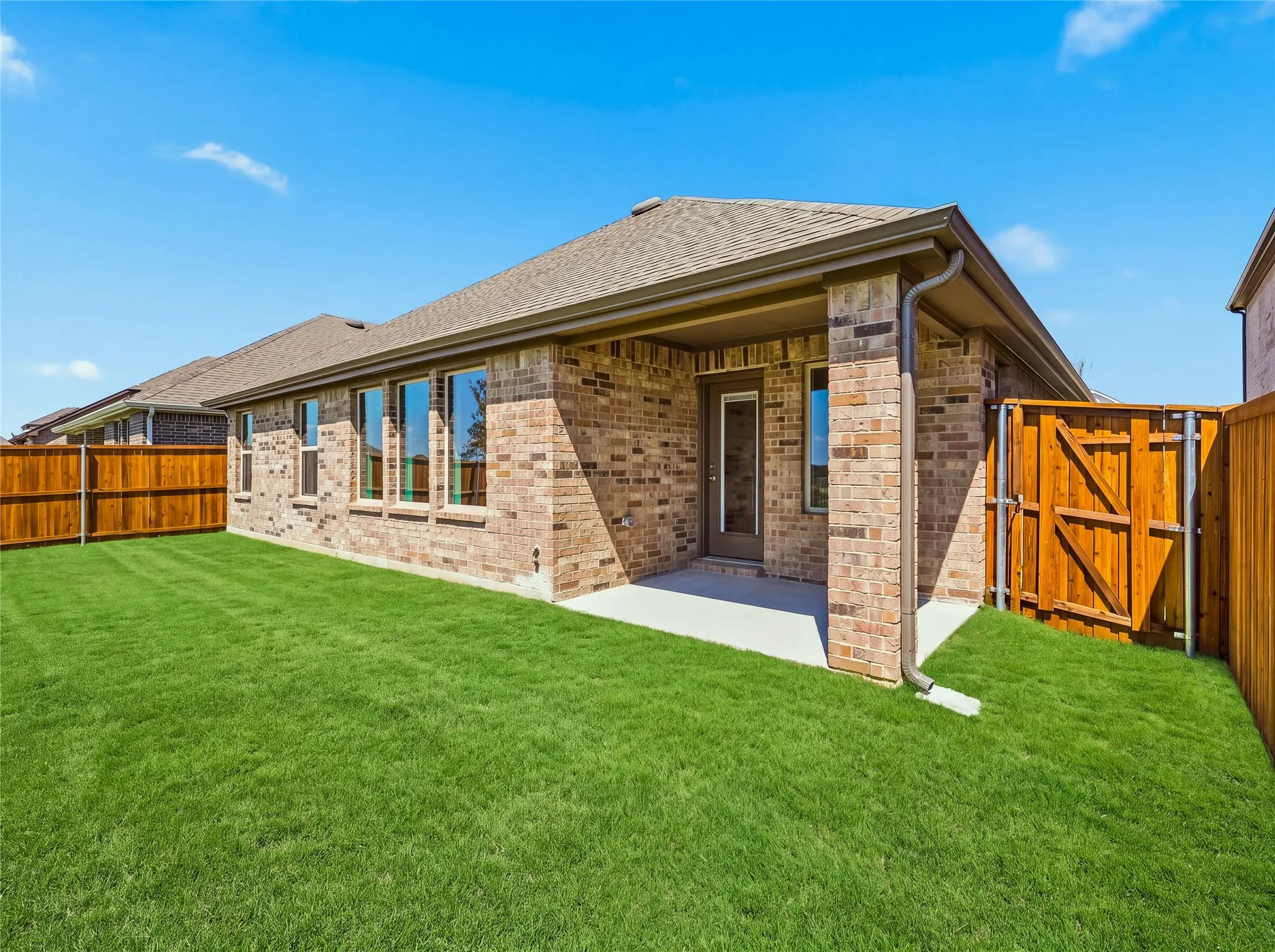Expansive grassy backyard featuring a covered patio, brick exterior, multiple windows, and a wood privacy fence
