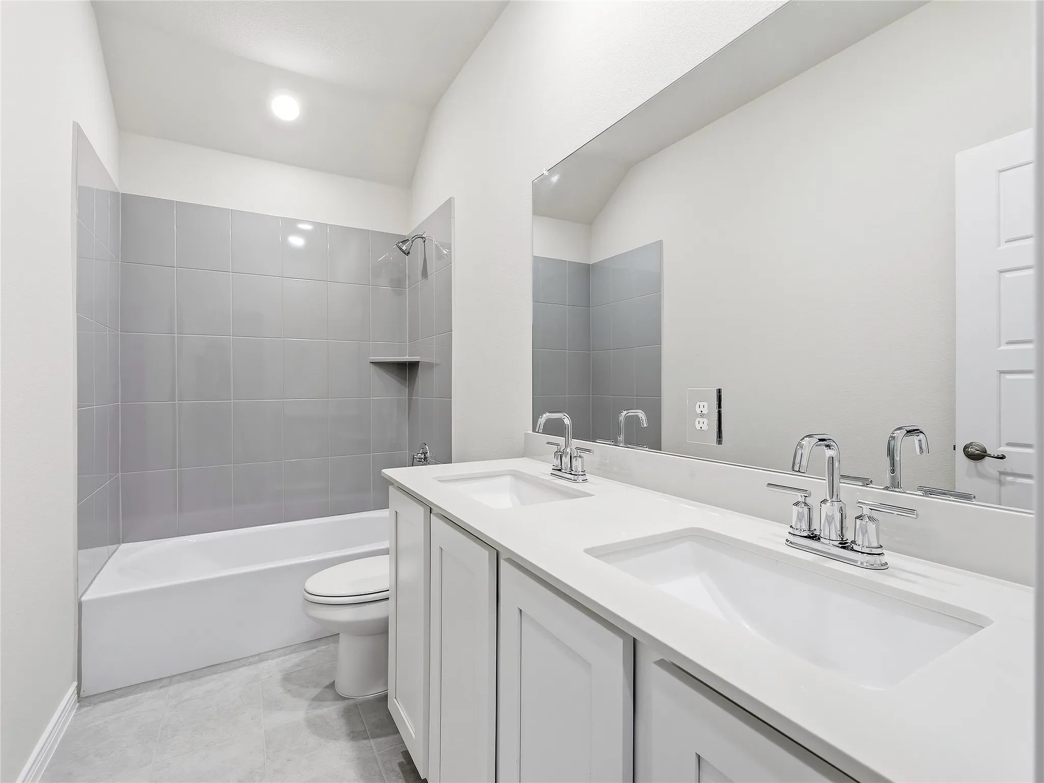 #2 Dual vanity with integrated sinks and chrome fixtures, a full-width mirror, tile flooring, and a tub with a tiled surround featuring a built-in niche