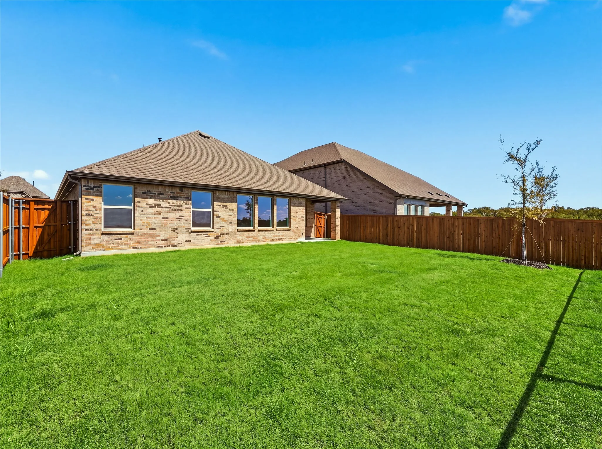 Expansive green lawn, wood privacy fencing, brick exterior, multiple windows, and a mature tree