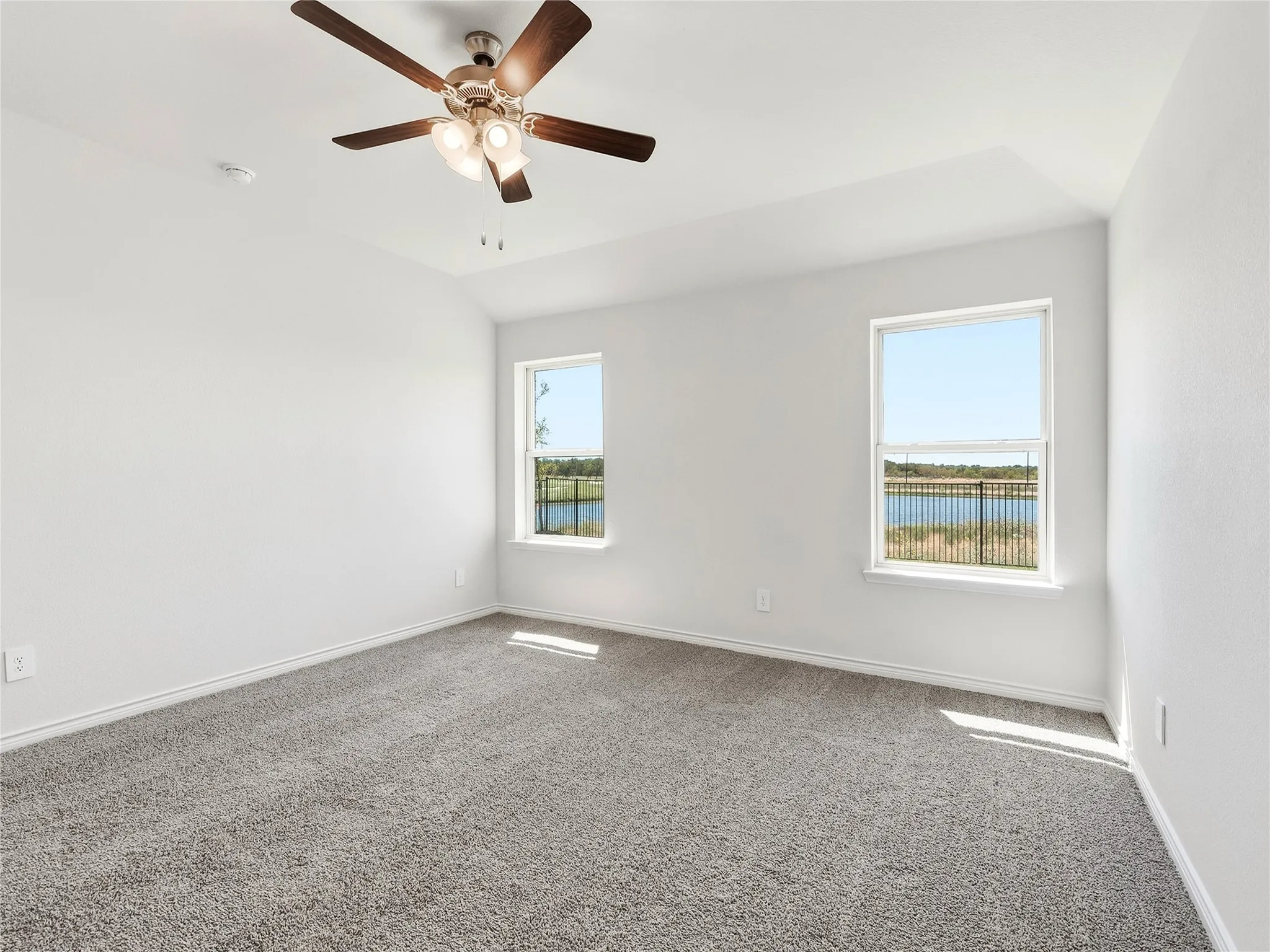 The serene lake scenery continues in the primary bedroom with plush carpet, ceiling fan with integrated lighting, and a tray ceiling