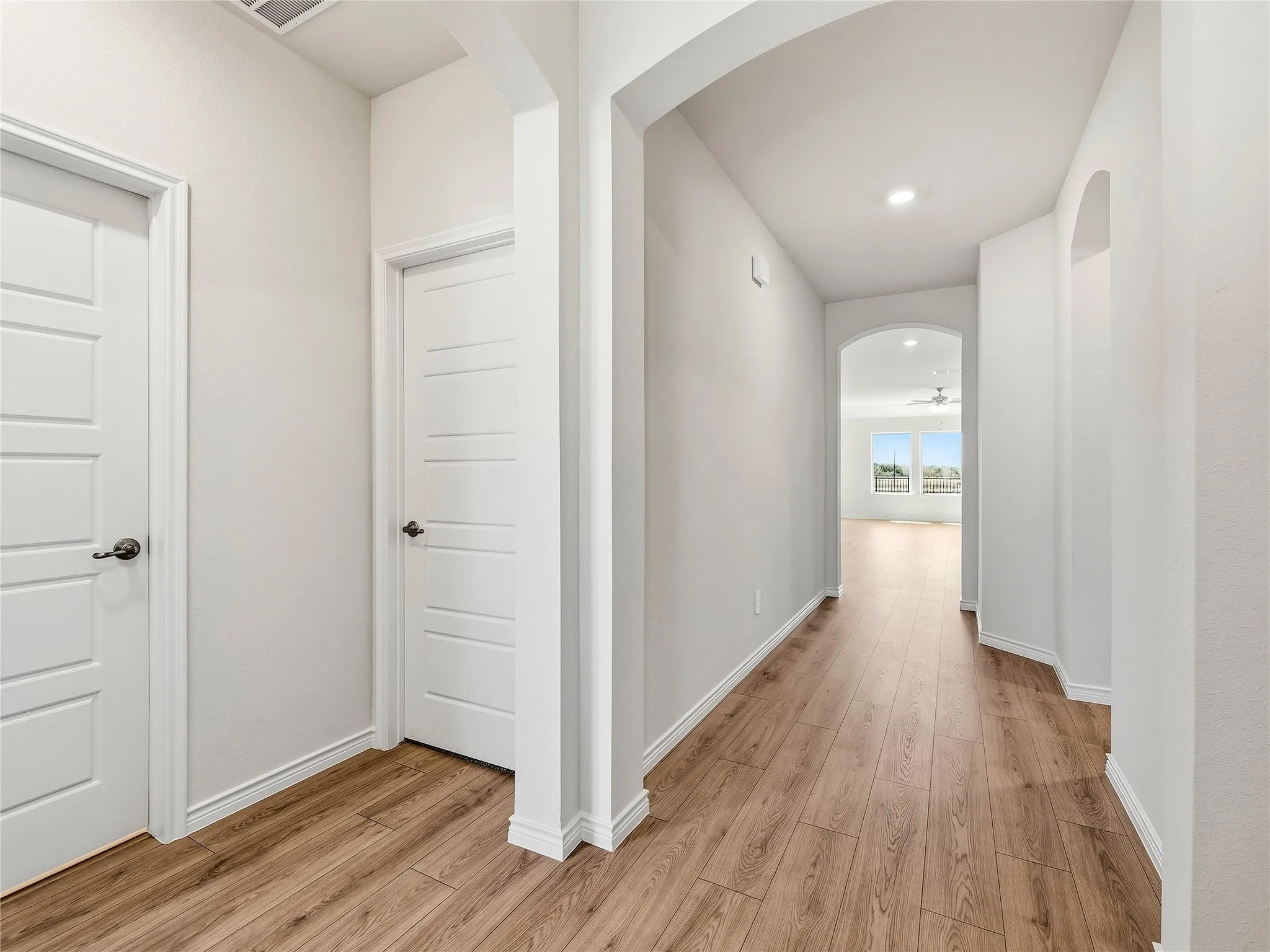 Wood-finish flooring throughout, bright white walls, recessed lighting, and arched doorways into a great lake view from kitchen, dining and living area