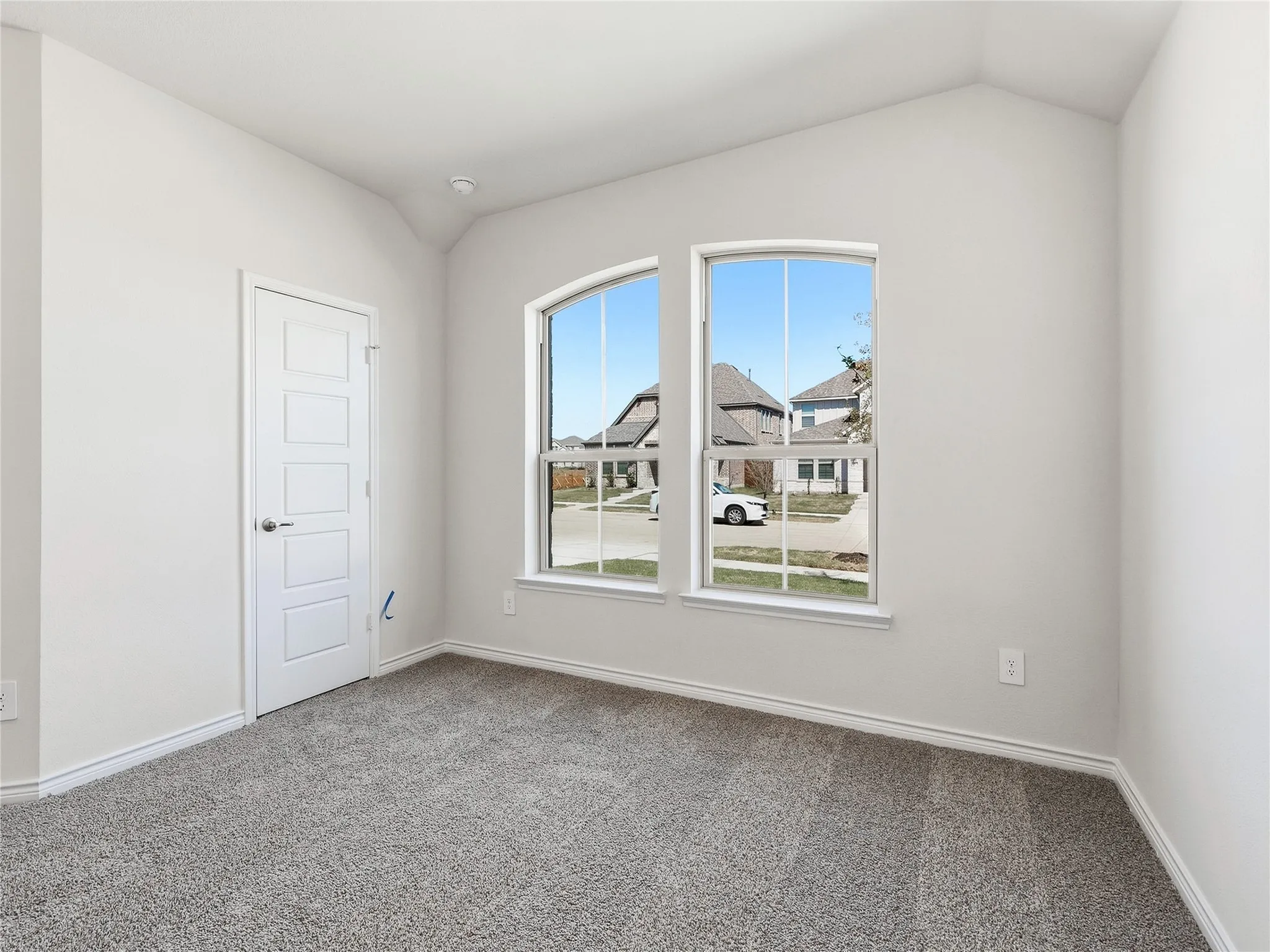 # 4 Vaulted ceiling with a flush-mount smoke detector, two arched windows, neutral-toned carpeting, and a five-panel interior door