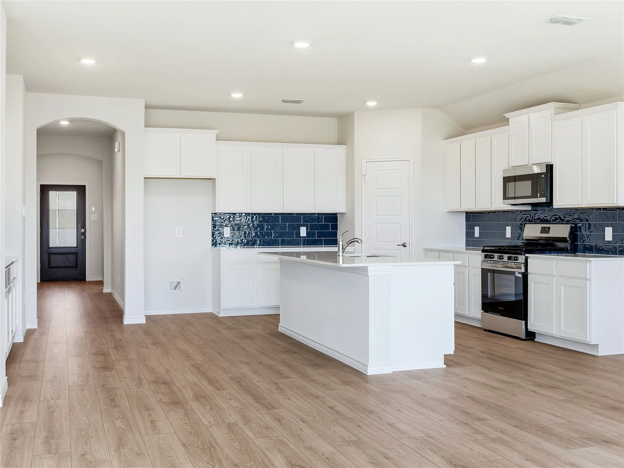 Ample cabinetry, stainless steel appliances, dark blue subway tile backsplash, walk in pantry, gas range, exhaust fan vents to the exterior.