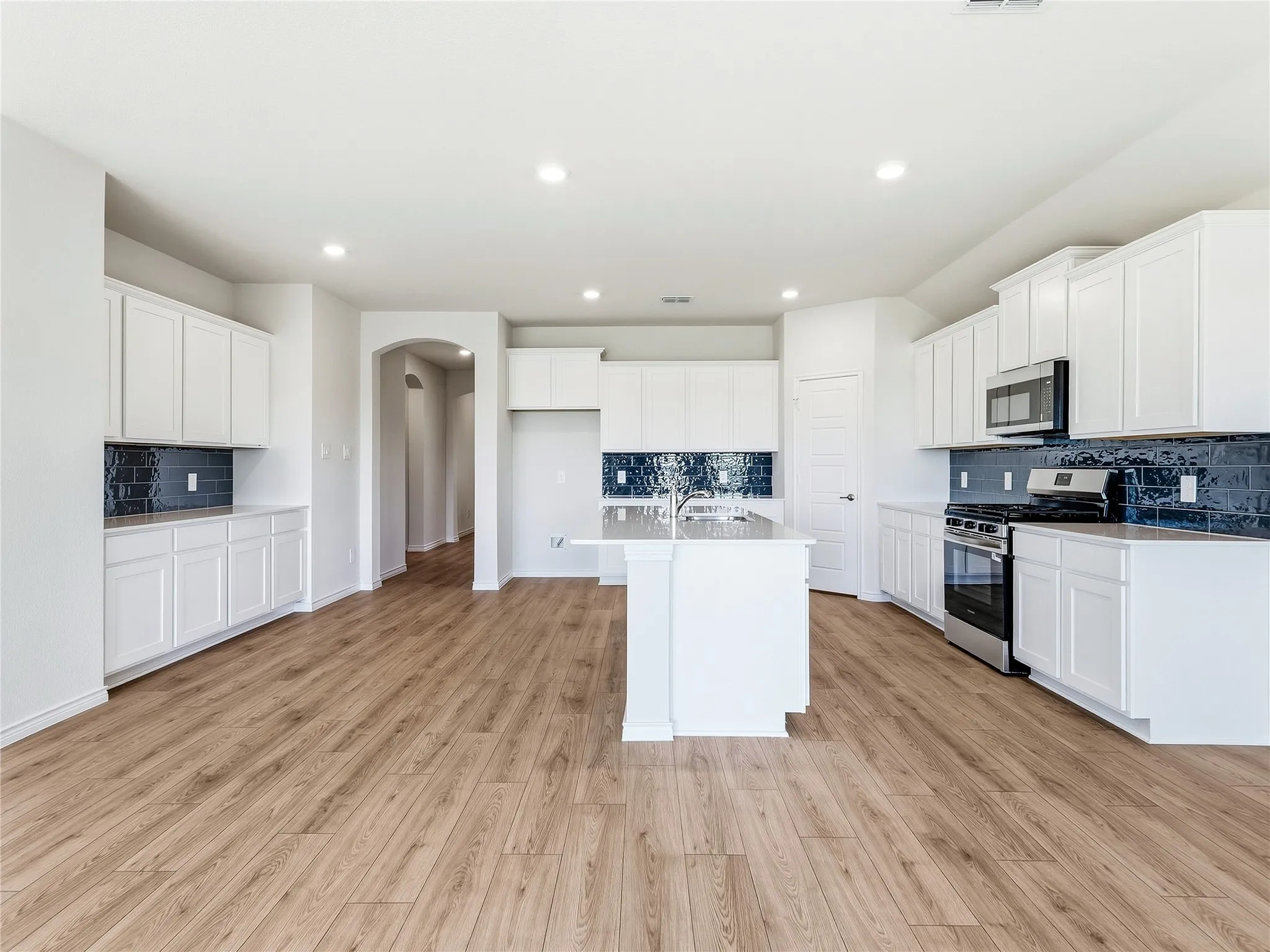 Open-concept kitchen with a central island, white cabinetry, integrated stainless steel appliances, and wood-finish flooring