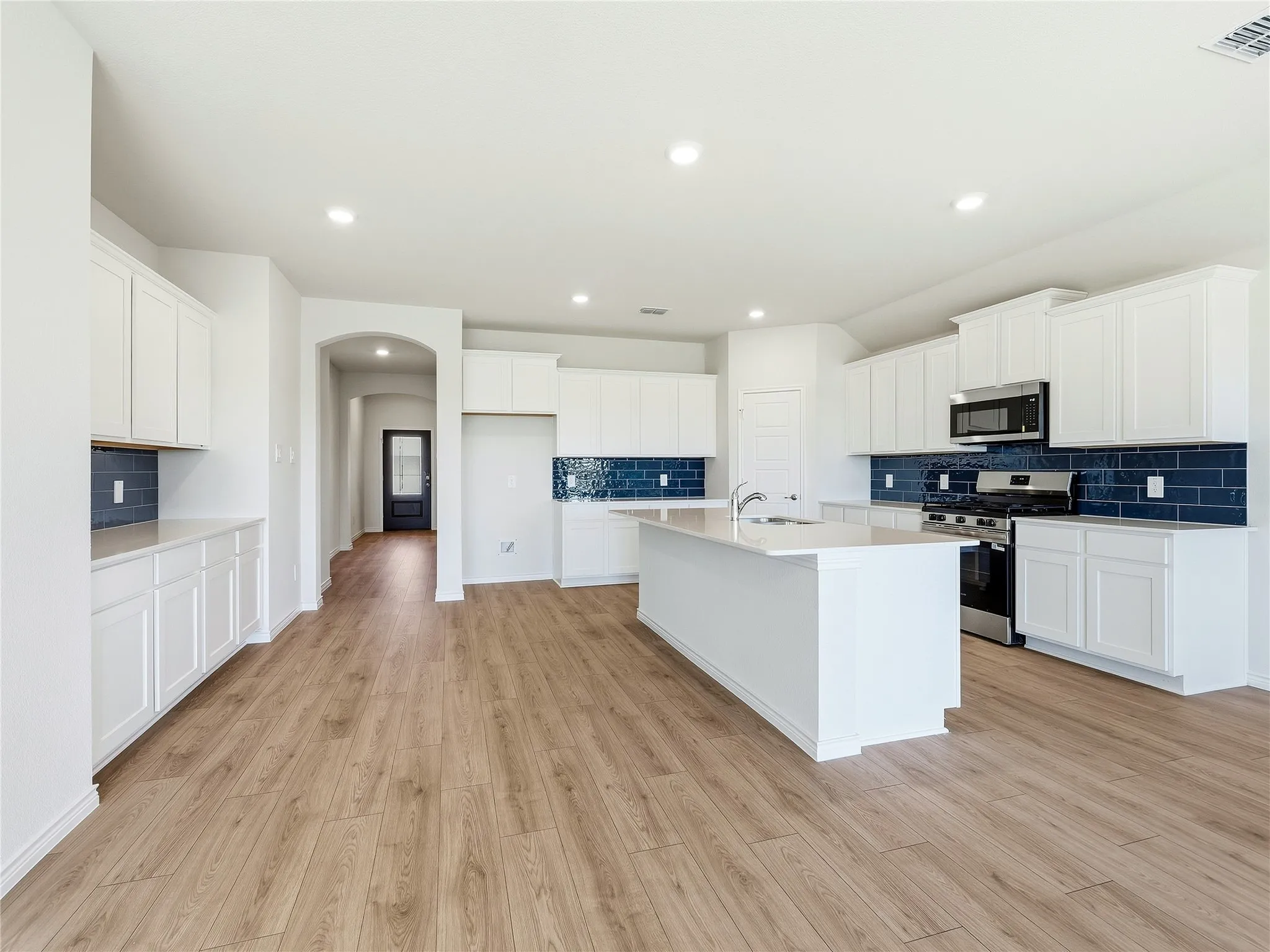 Open-concept kitchen with wood-finish flooring, white cabinetry, dark blue subway tile backsplash, stainless steel appliances, and a central island