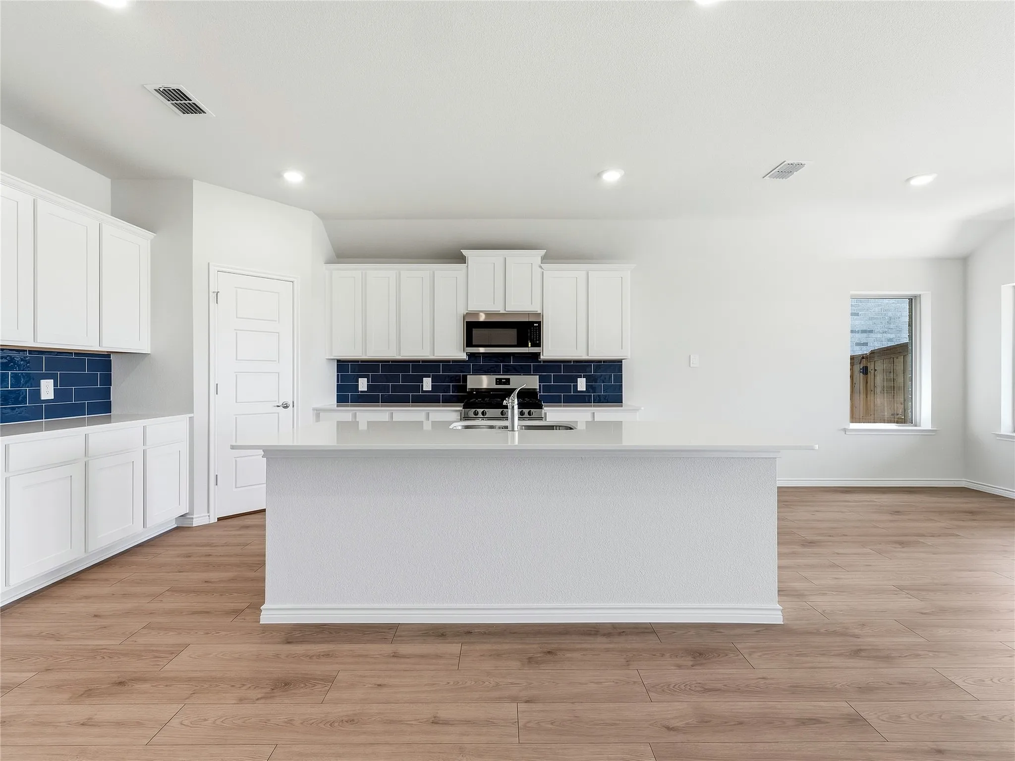 Large central island, white countertops, and a blue subway tile backsplash