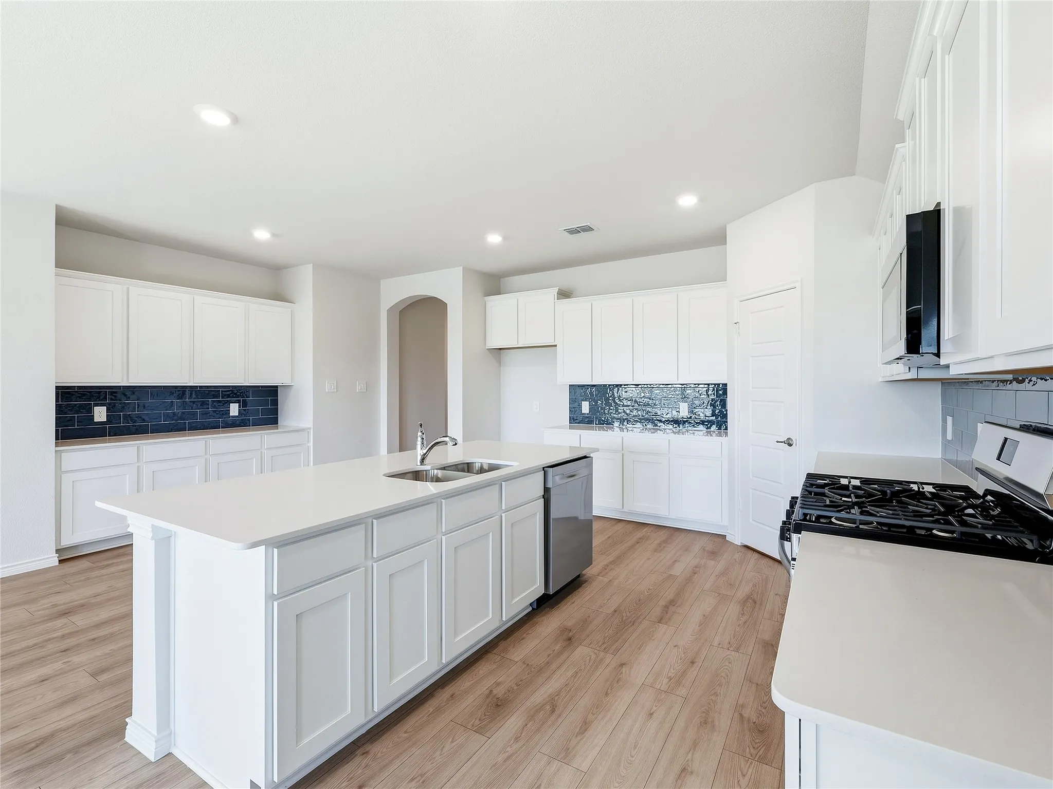 Well-appointed kitchen featuring light wood-finish flooring, white cabinetry, dark subway tile backsplash, a center island with a double basin sink, and stainless steel appliances