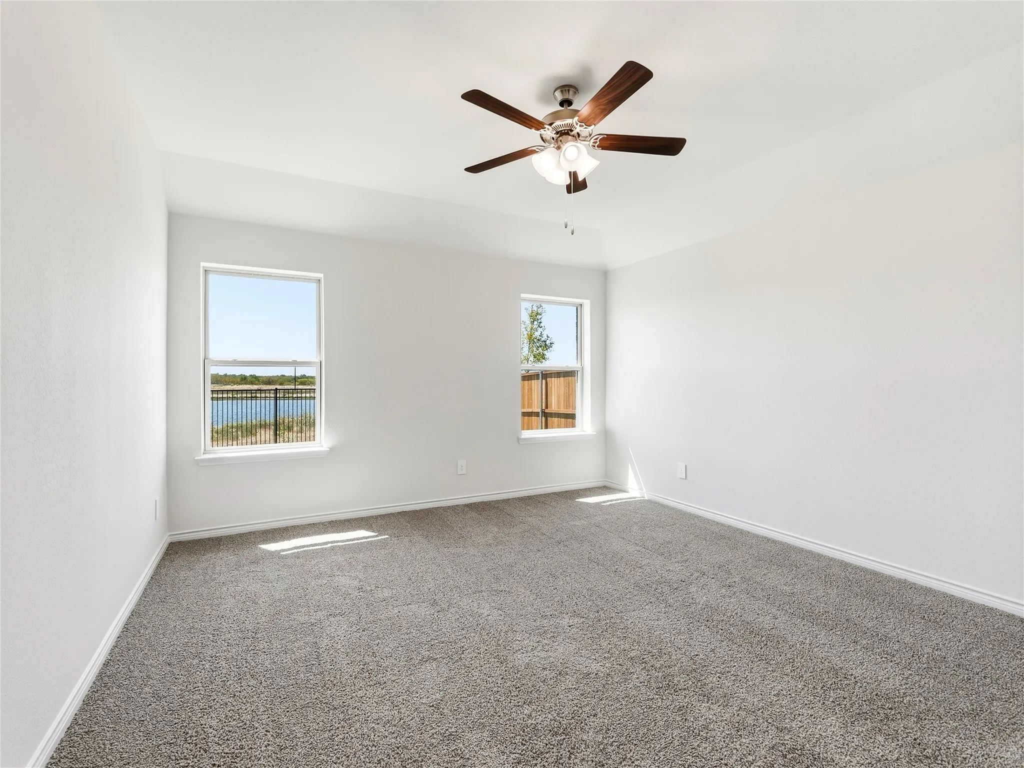 Spacious room featuring neutral carpet, two windows with outdoor scenery, and a ceiling fan with integrated lighting