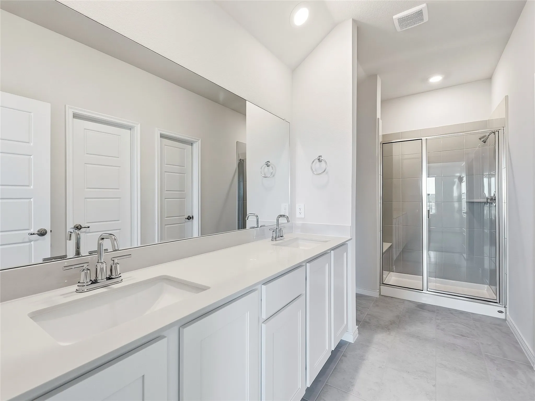 Dual vanity with integrated sinks, expansive mirror, tiled flooring, and a glass-enclosed shower with tiled walls and a built-in bench