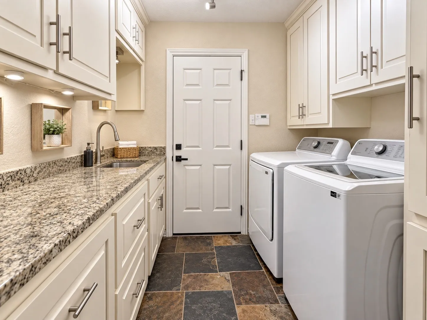 Laundry room featuring extensive white cabinetry, a stainless steel sink, granite countertops, and slate tile flooring