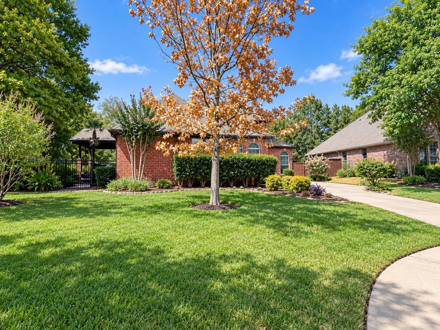 Brick exterior residence with arched windows, an attached two-car garage, mature landscaping, and a fenced side yard with a pergola