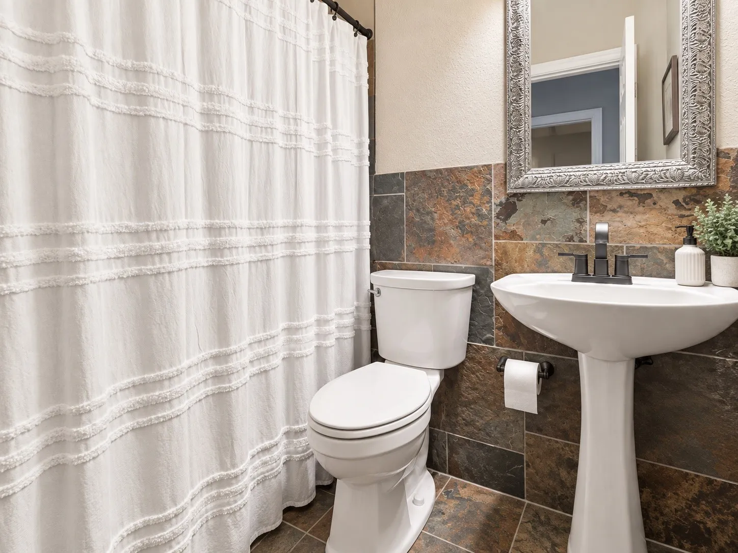 Pedestal sink with a matte black faucet, wall-mounted mirror, and multi-toned tile wainscoting