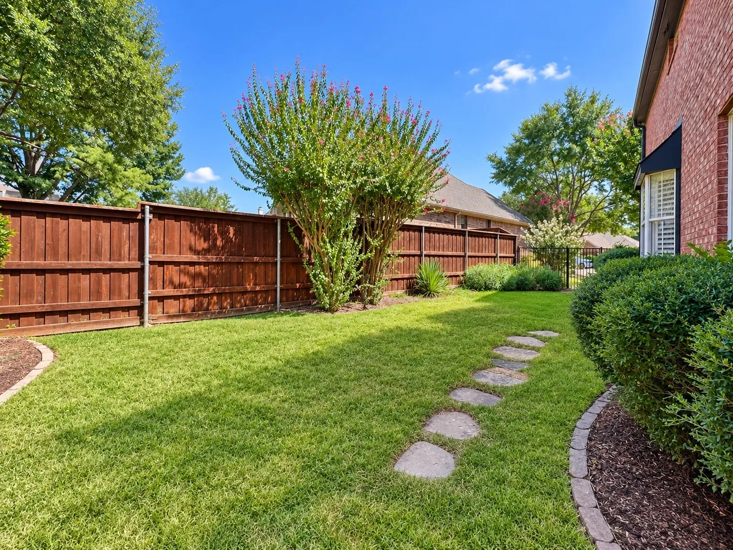 Expansive lawn with a stepping stone pathway, complemented by a wood privacy fence and established landscaping