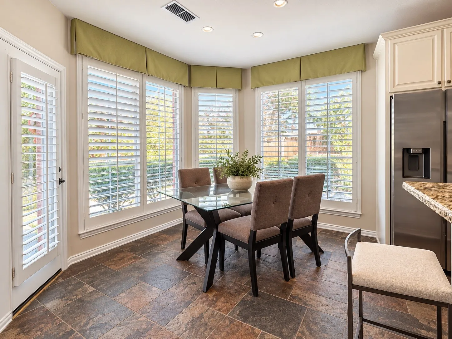 Bay window with plantation shutters, tile flooring, recessed lighting, and a stainless steel refrigerator