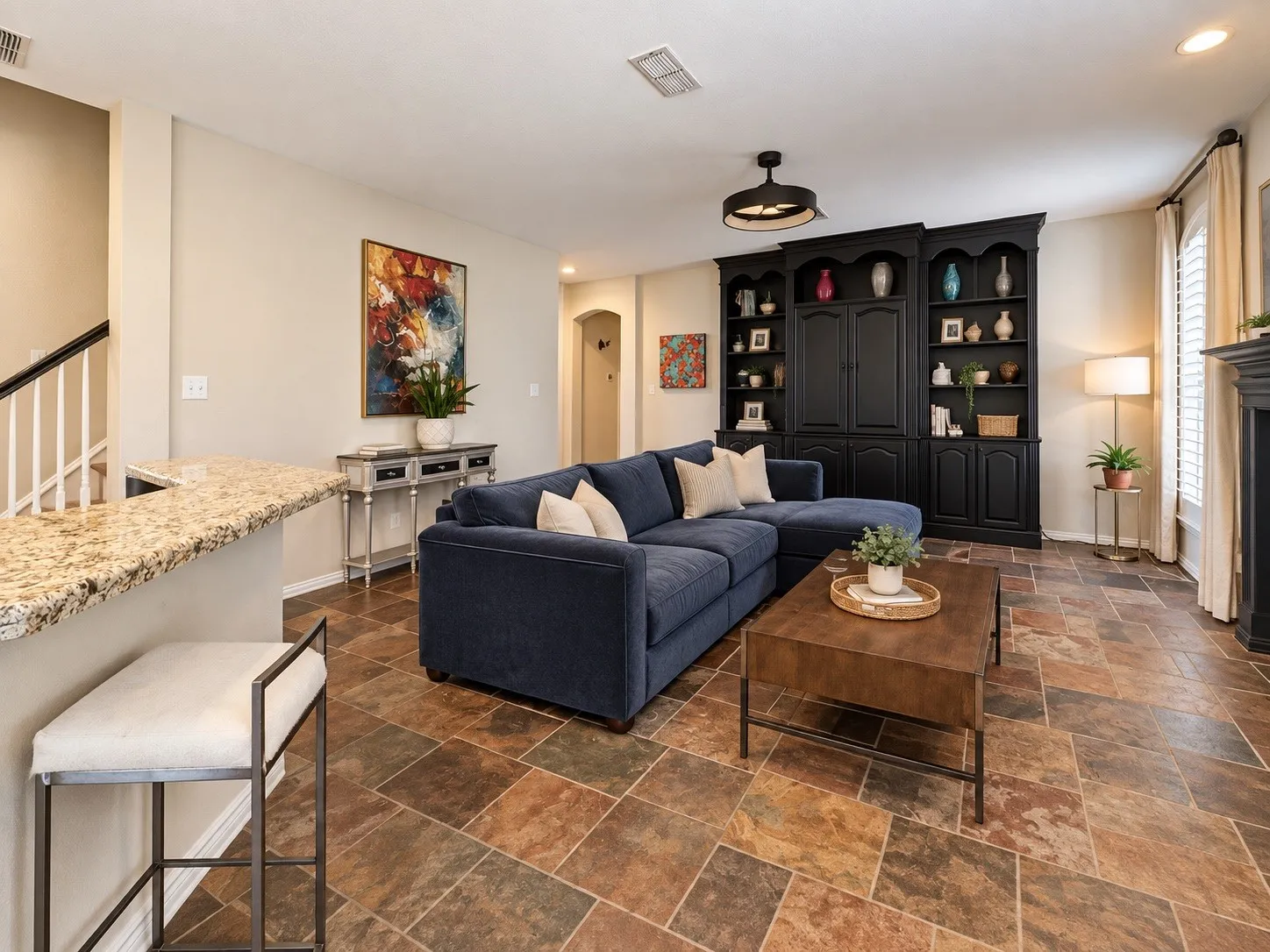 Built-in shelving unit, multi-tone tile flooring, breakfast bar with stone countertop, staircase with white spindles, and window with plantation shutters