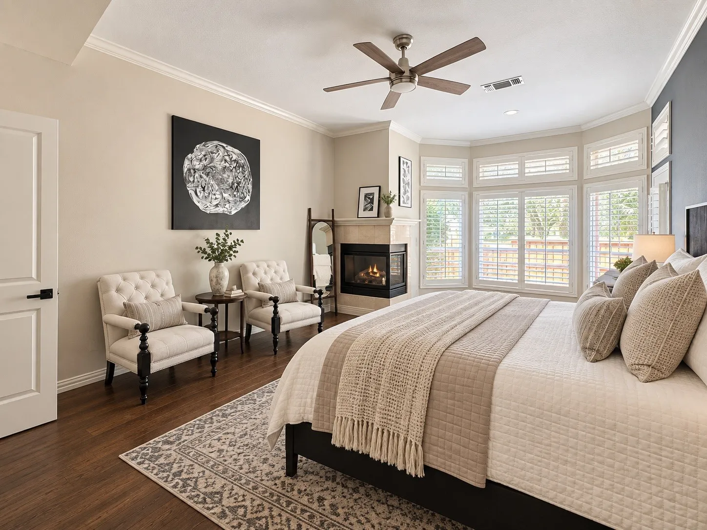 Hardwood-finish flooring, crown molding, bay windows with plantation shutters, corner fireplace with stone surround, and a ceiling fan with integrated lighting