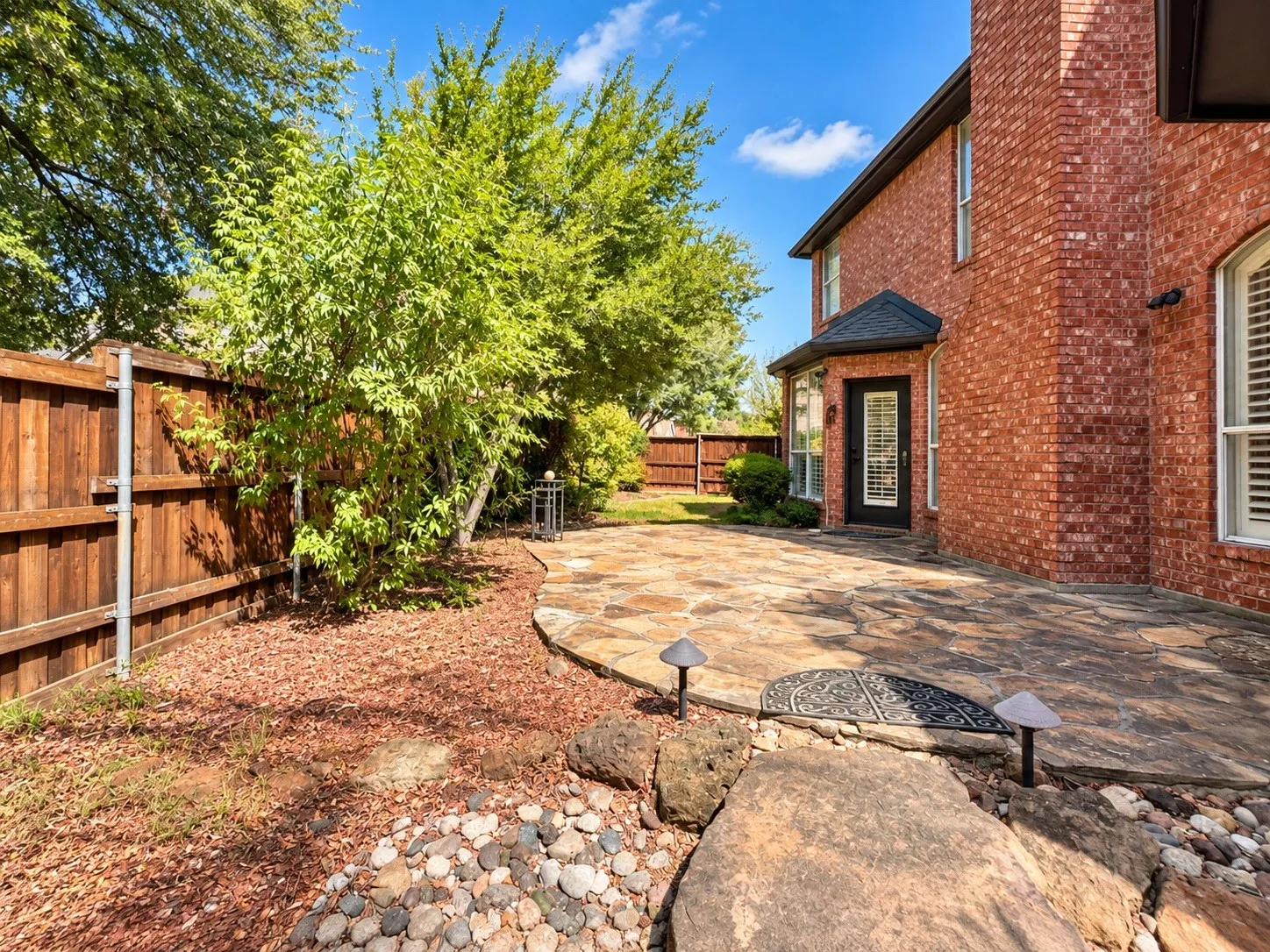Brick exterior with a covered entry, flagstone patio, and mature trees